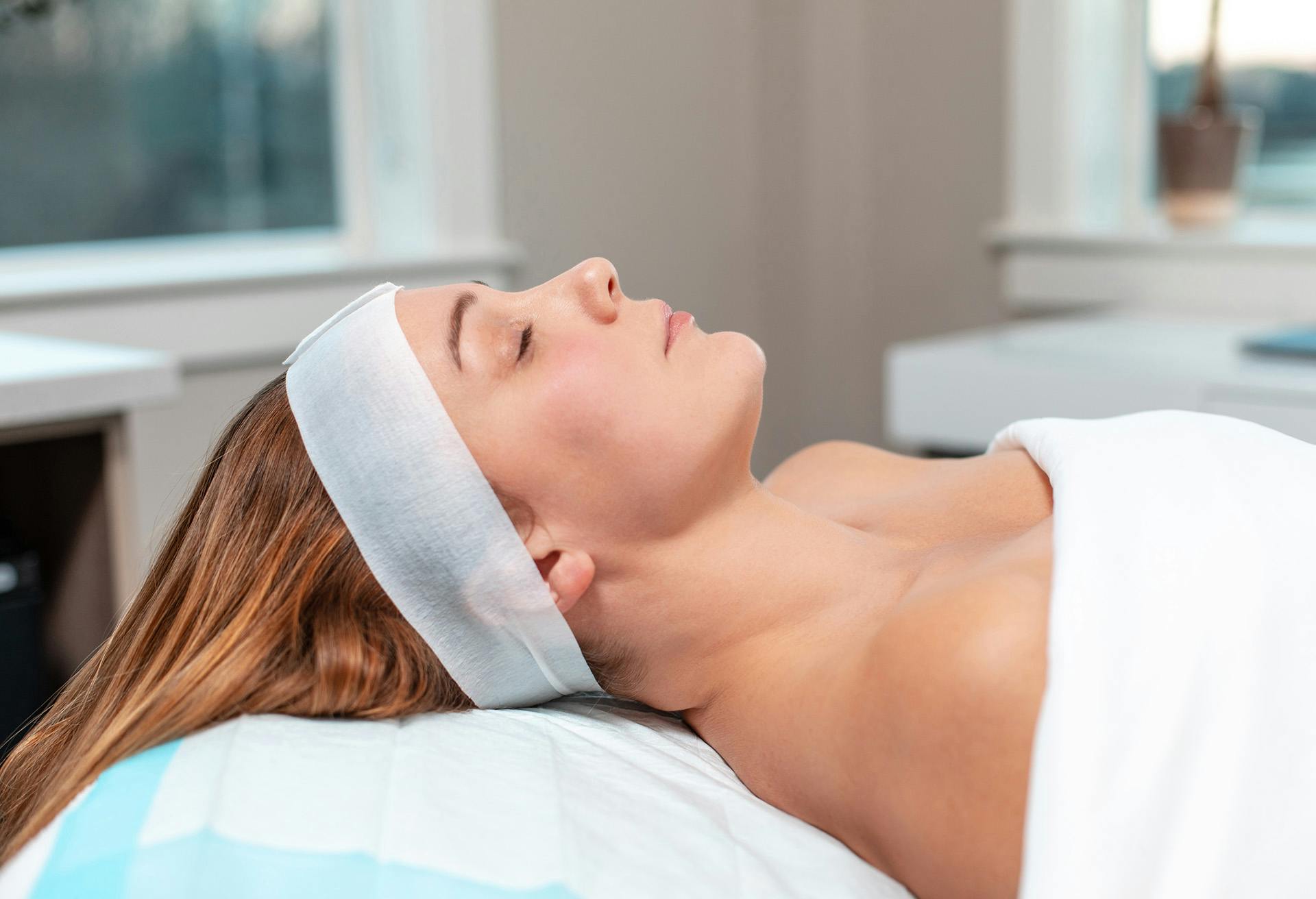 A woman laying on an exam chair about to get a facial