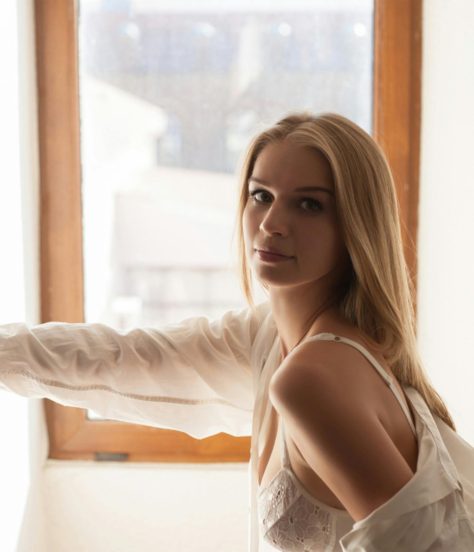 blond woman in white dress leaning against window with arm outstretched