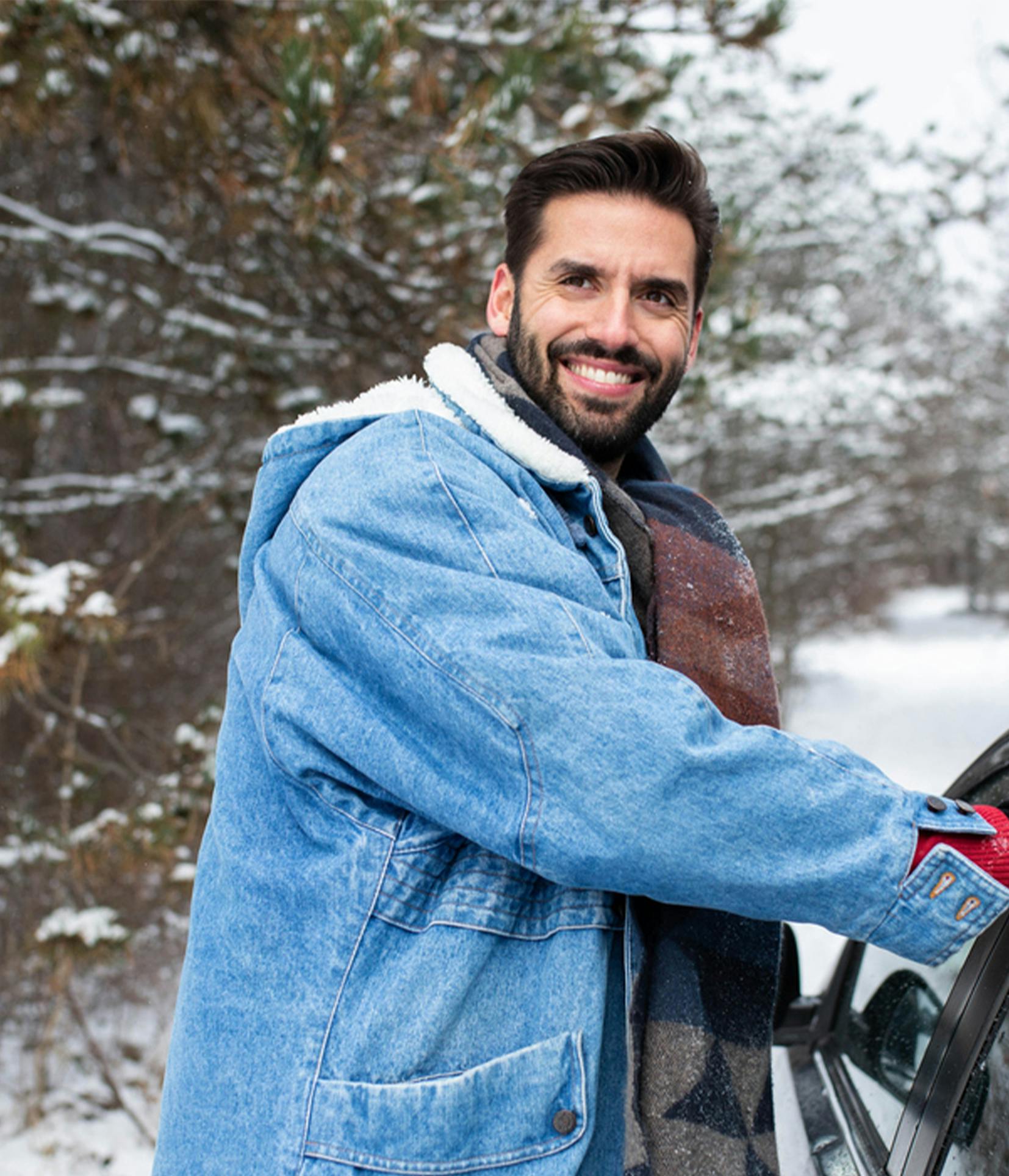 smiling man in winter coat leaning on car window with snow on ground
