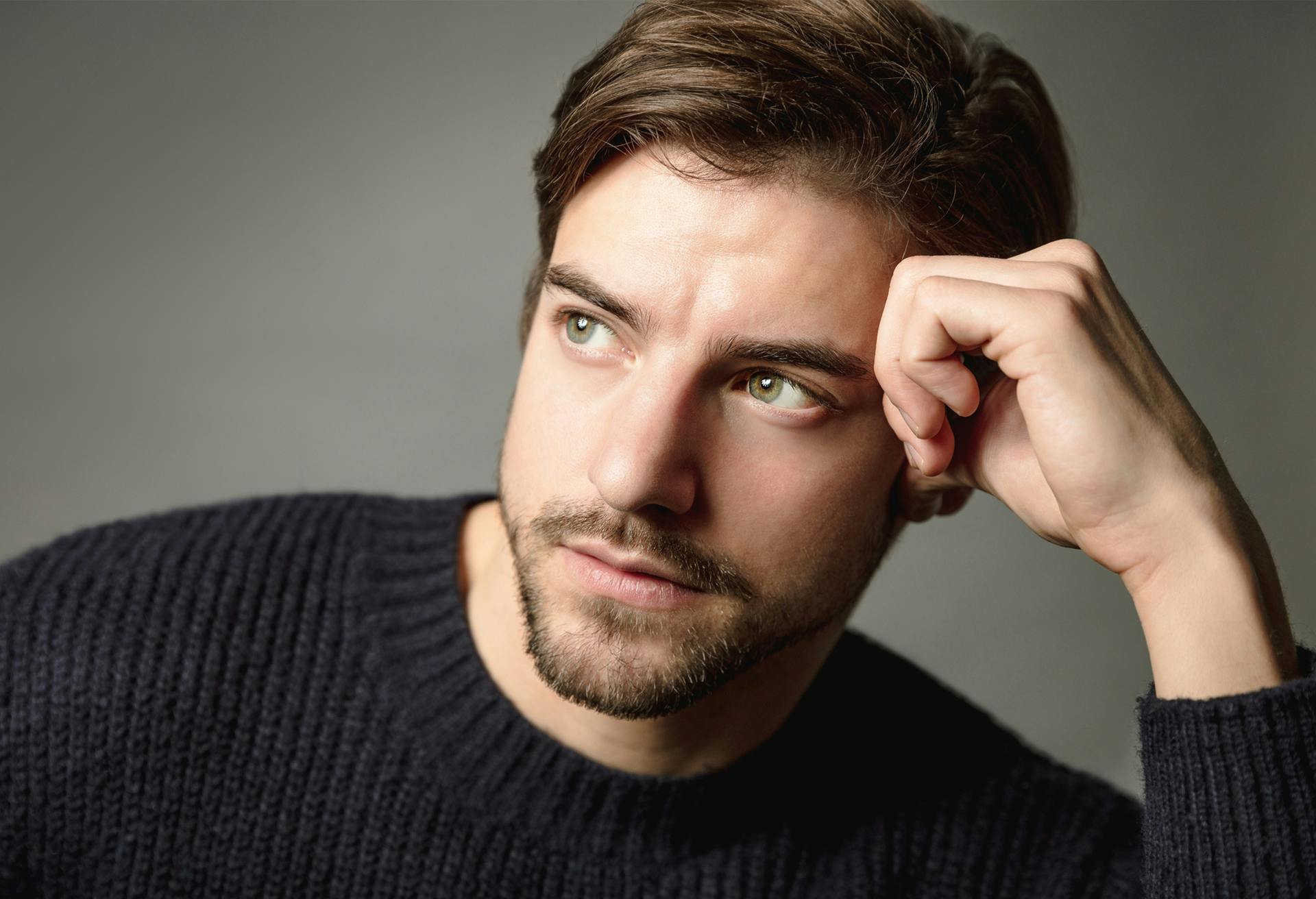 A man in a sweater resting his head in his hand