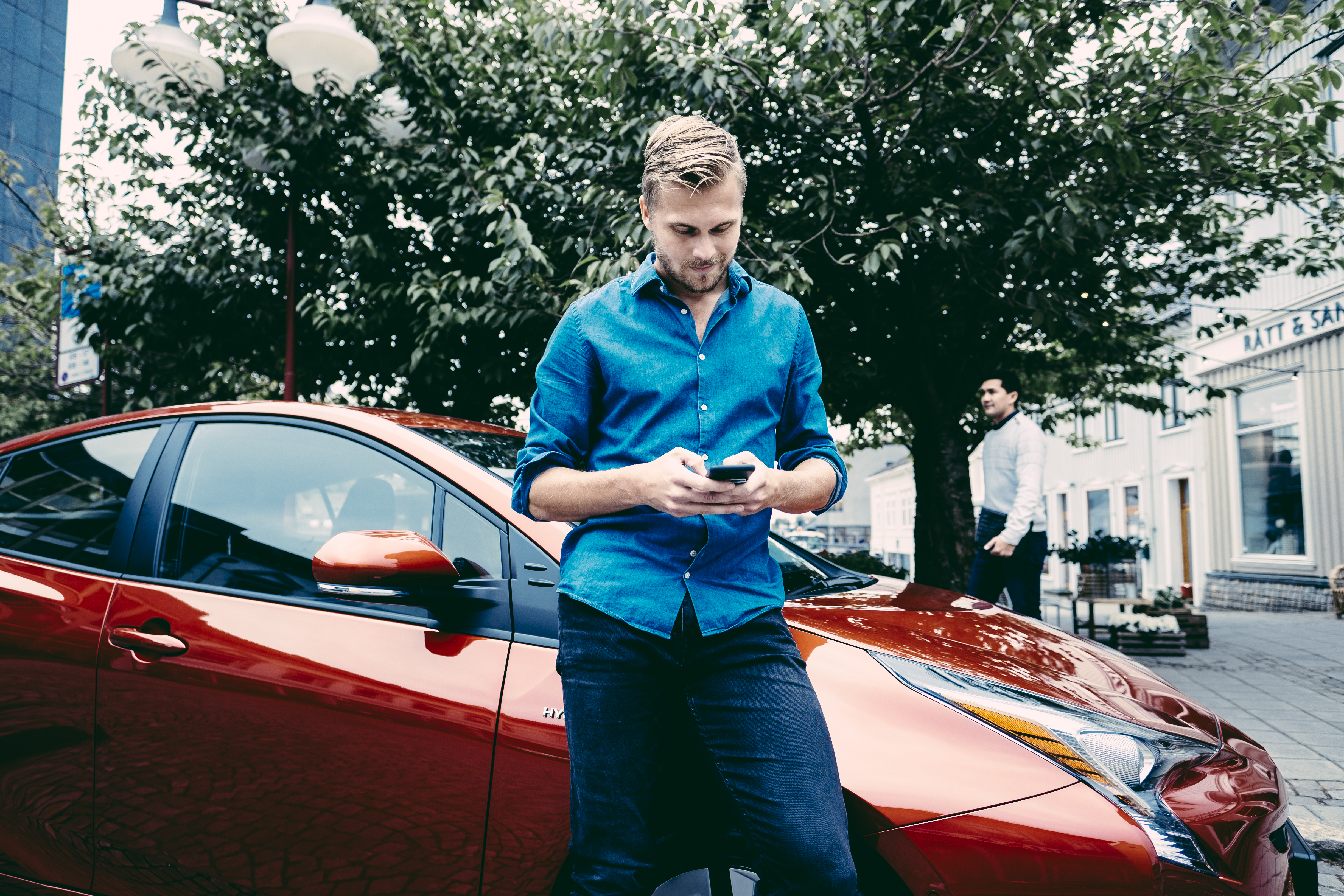 Man on phone standing in front of orange car