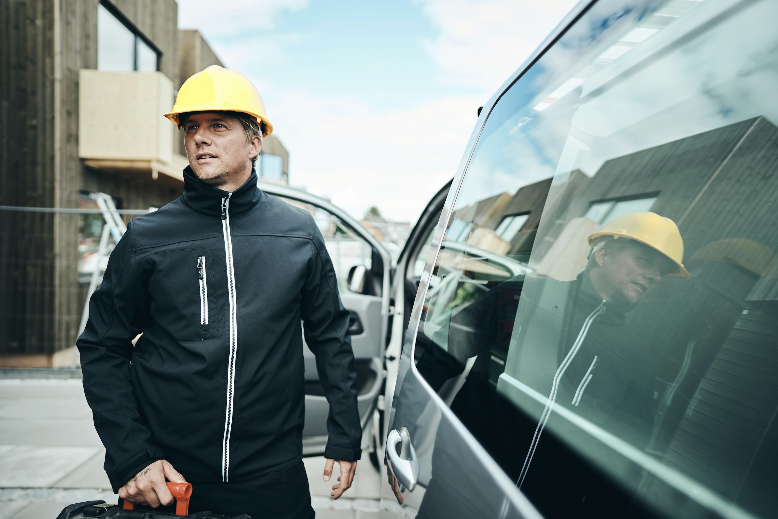 Mannelijke bouwvakker met veiligheidshelm naast bestelwagen