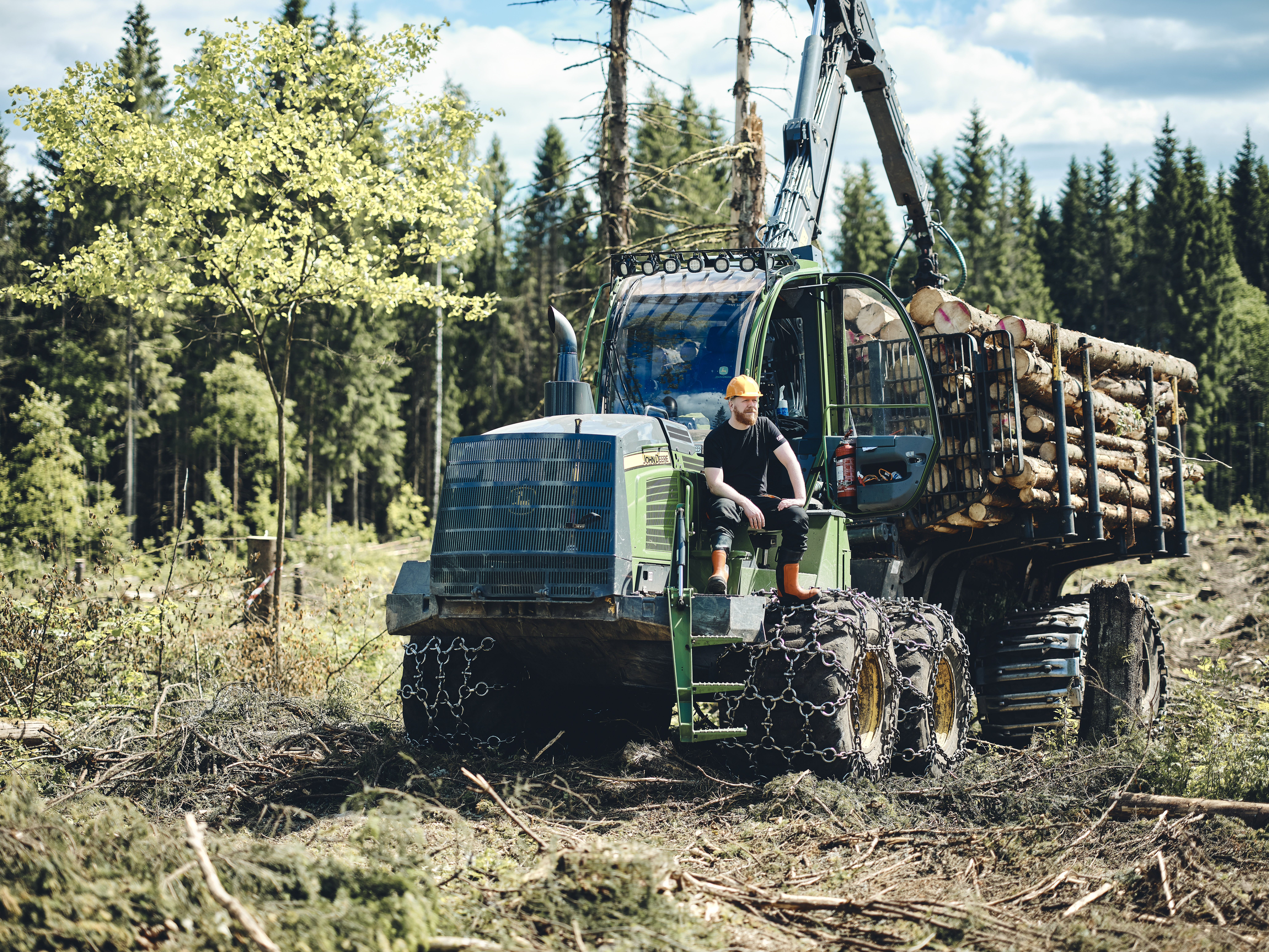 Farmer sitting on tractor with wood logs in the forest
