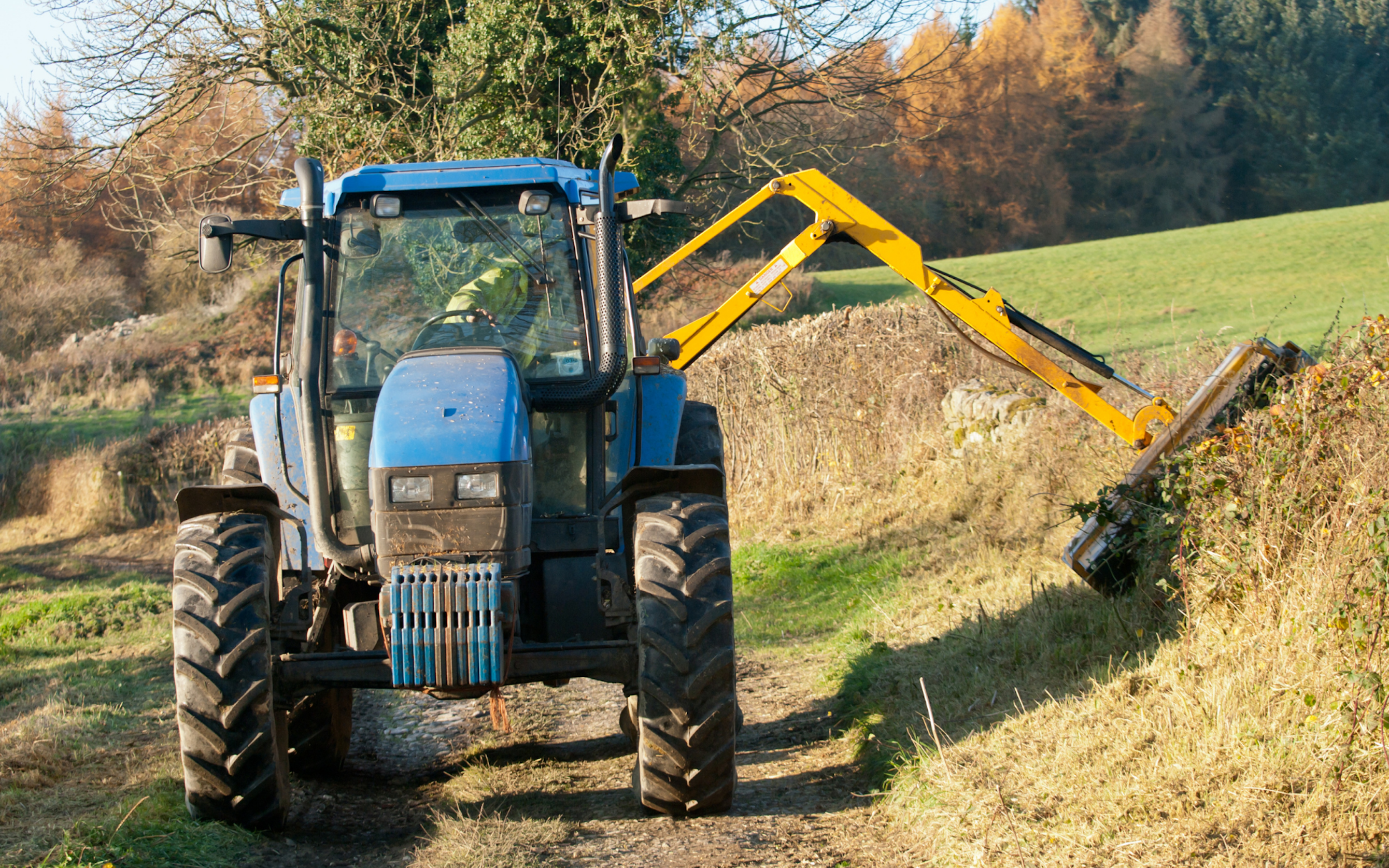 Blauwe tractor die de haag snoeit