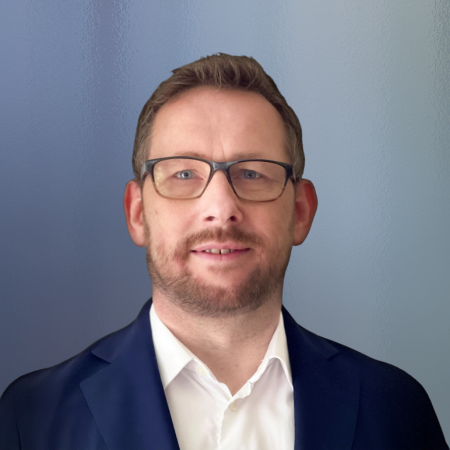 Headshot of man with glasses in suit blurred grey background