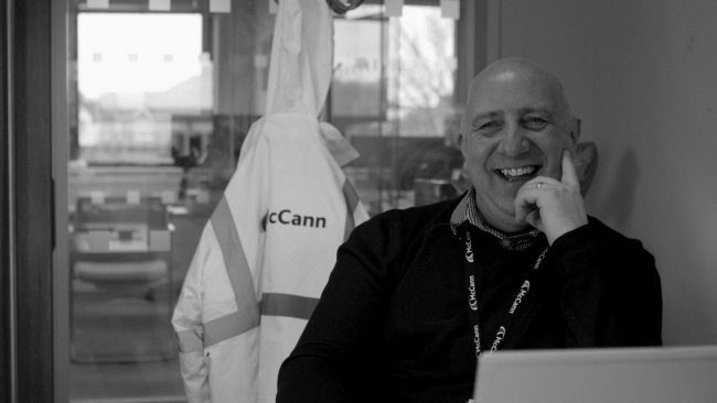 Zdjęcie w czerni i bieli przedstawiające siedzącego w biurze mężczyznę, pracownika firmy McCann Ltd.