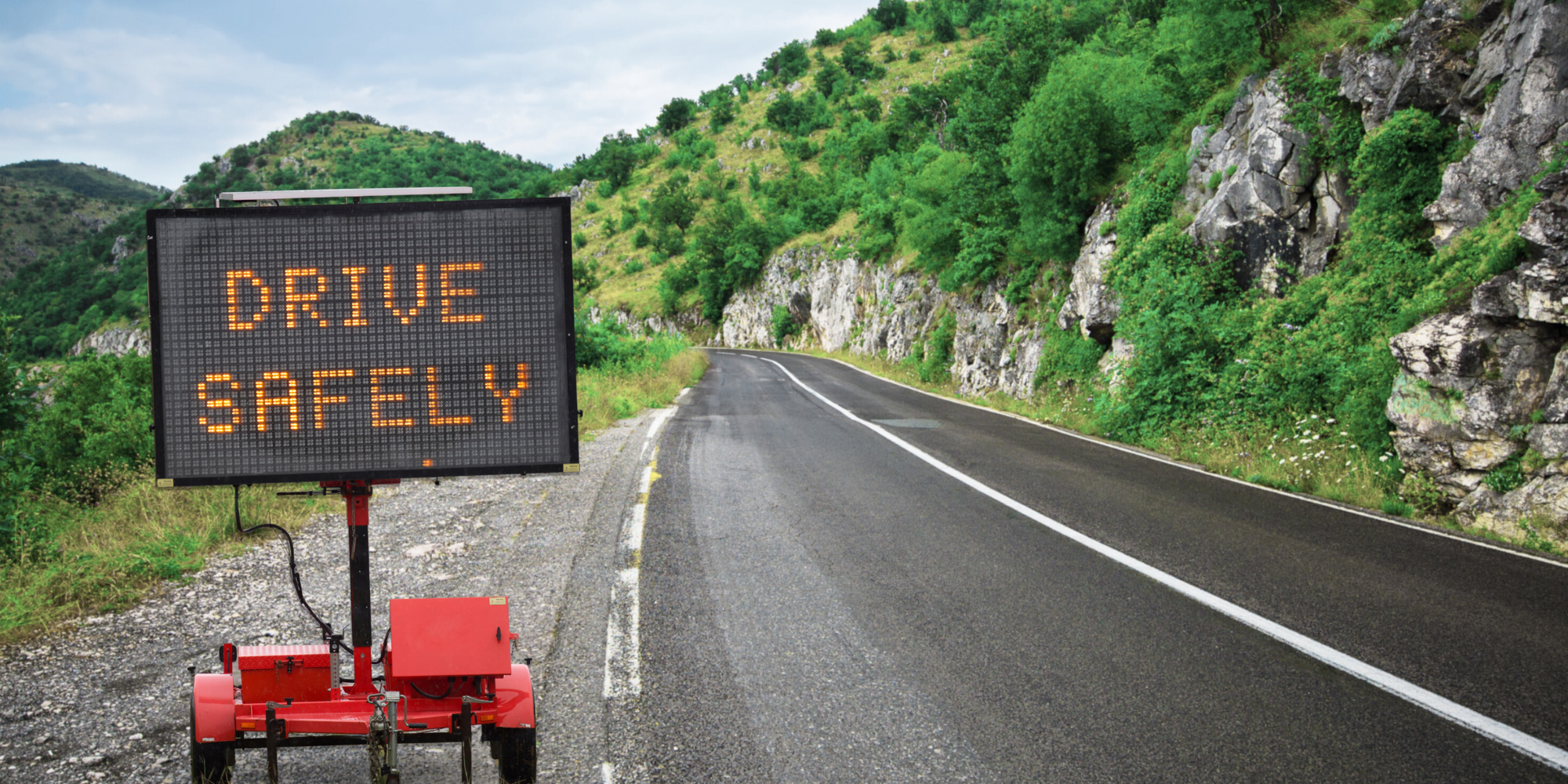 Drive safely road sign on country road side with hills and trees in the background