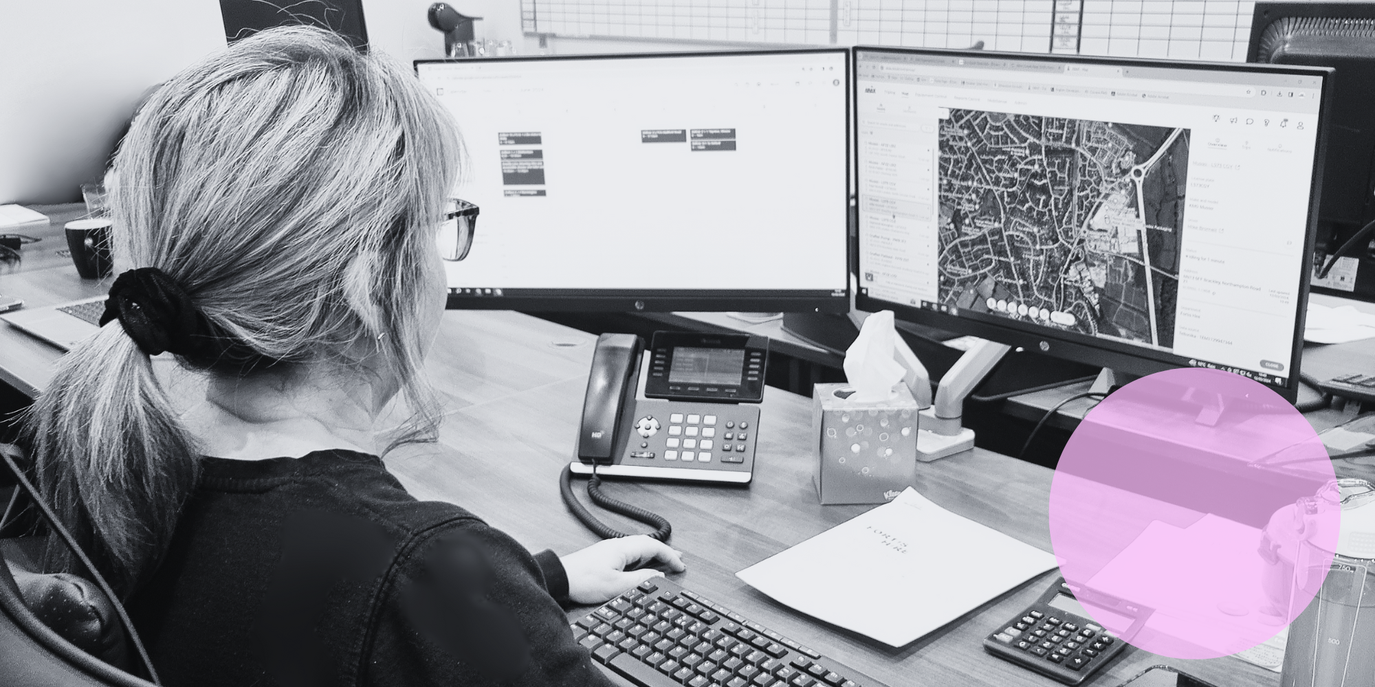 Black and white picture of woman sat at desk and looking at the ABAX app on screen