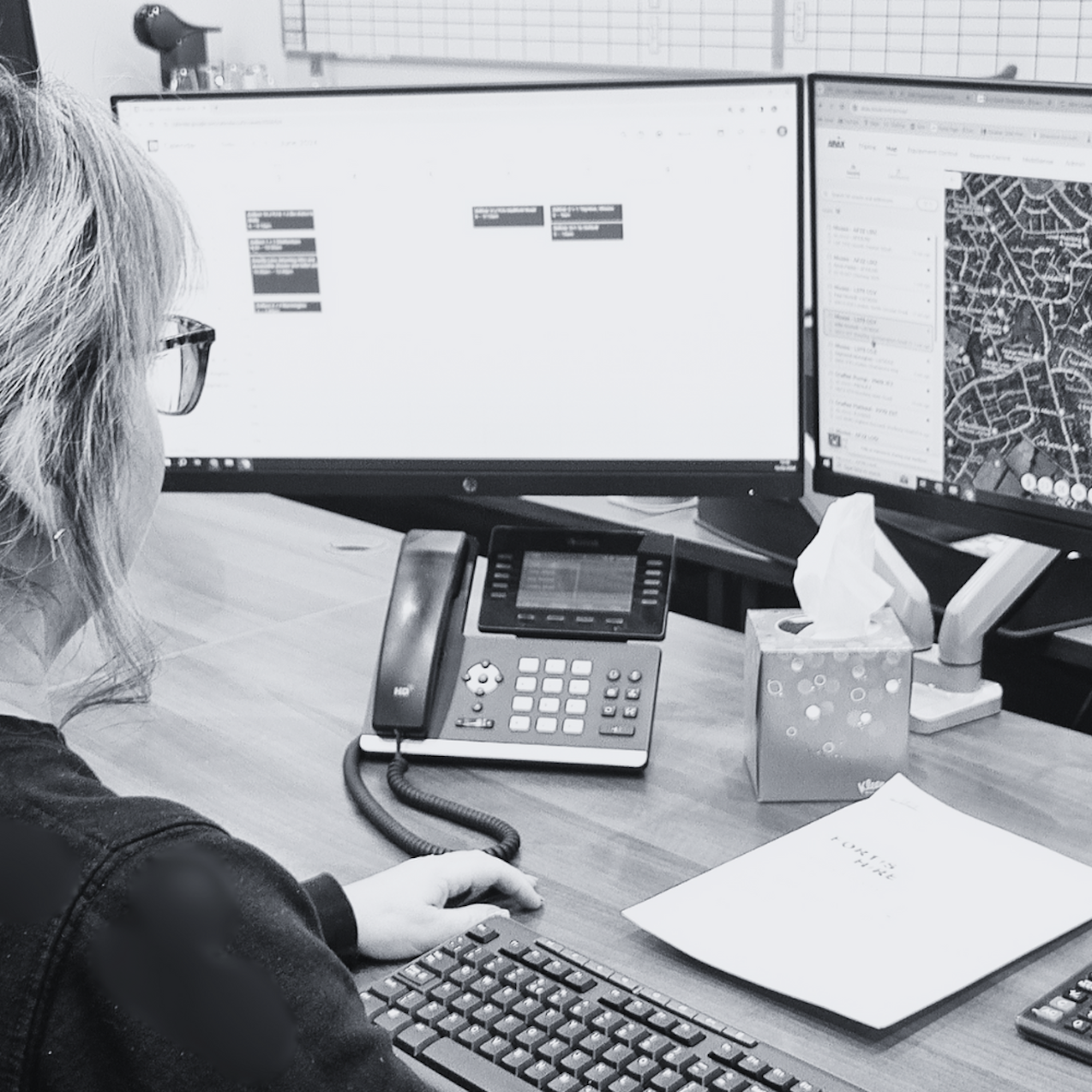 Black and white picture of woman sat at desk and looking at the ABAX app on screen