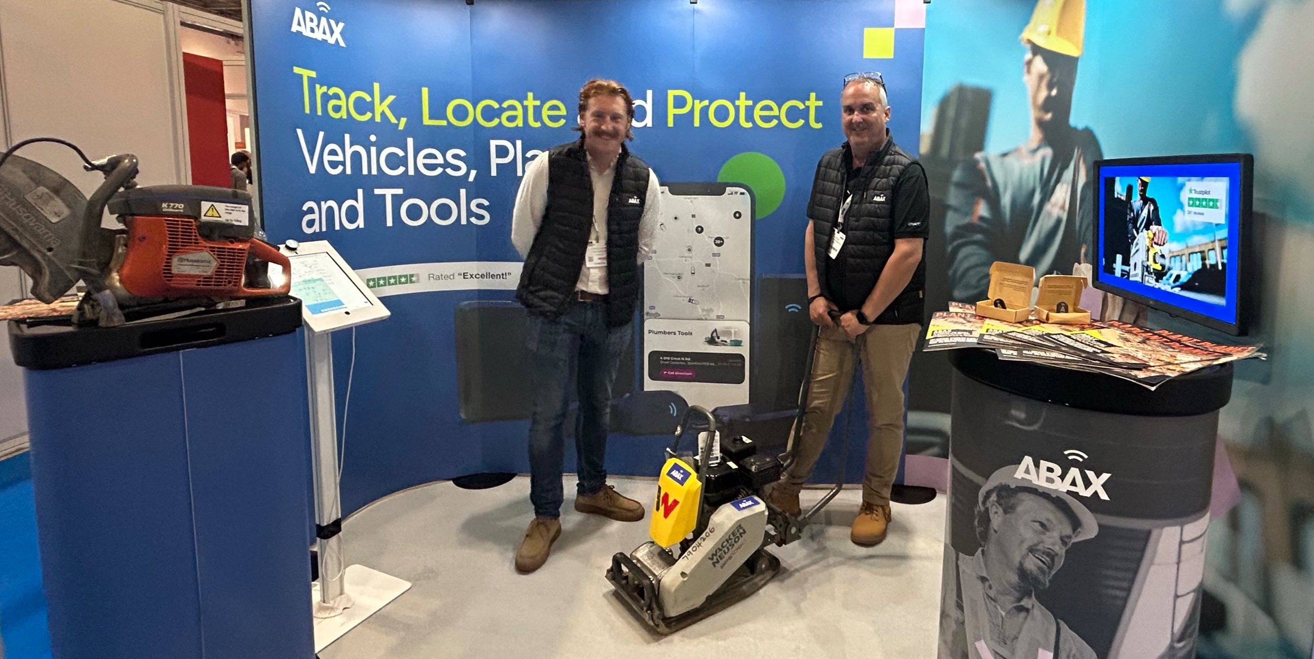 Exhibition stand at UK Construction Week with 2 ABAX members standing in the middle.