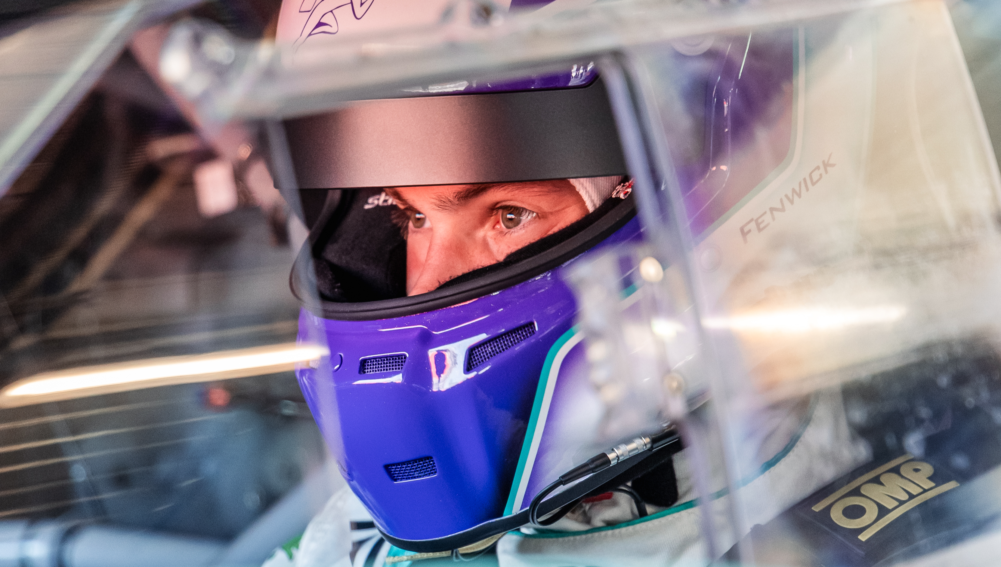 Close up of racing car driver Fraser Fenwick inside car with purple and white helmet