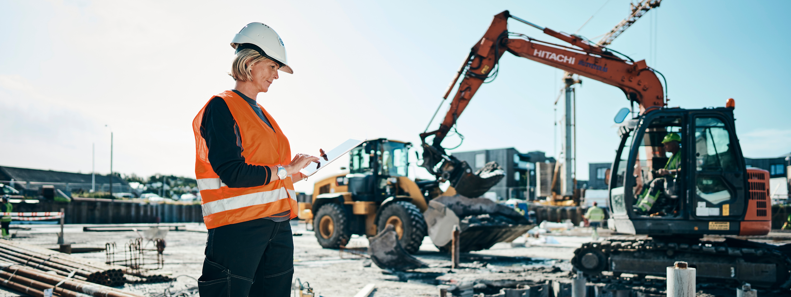 Woman construction worker in high vis, standing in front of machinery
