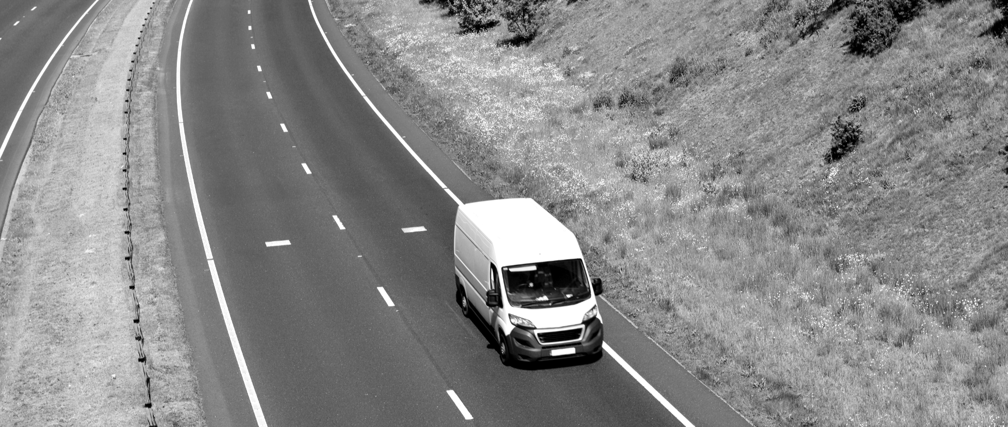 Black and white picture of a van driving on a dual carriageway in the countryside