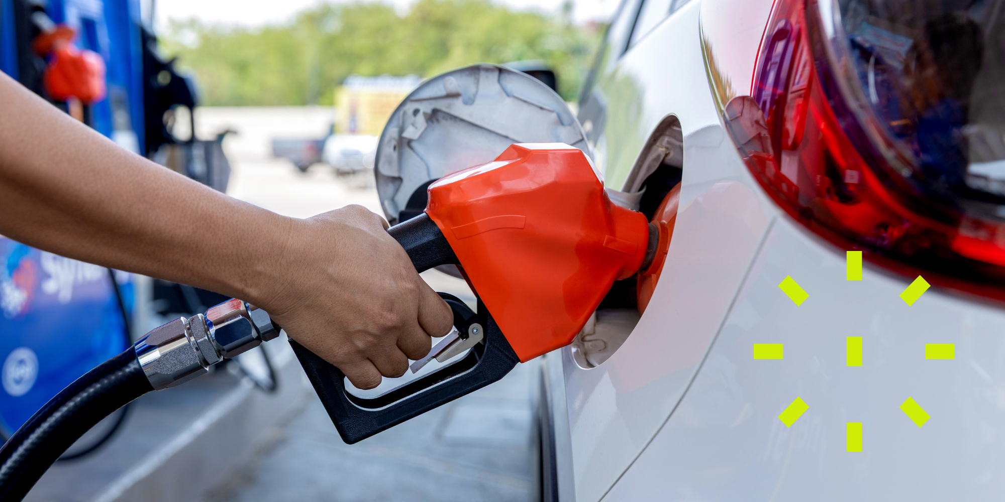 Fuel station - Petrol pump in orange and black in white car with trees in the background