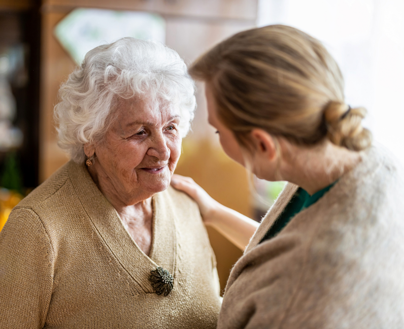 Older lady in beige top with a younger carer in a cream cardigan