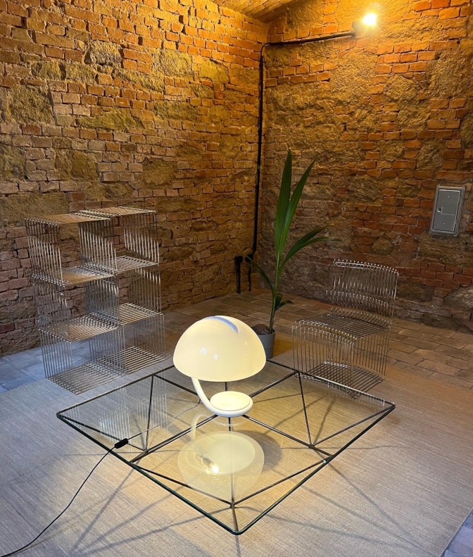 weiße Lampe und gläserne Beistelltische vor einer beleuchteten Backsteinwand