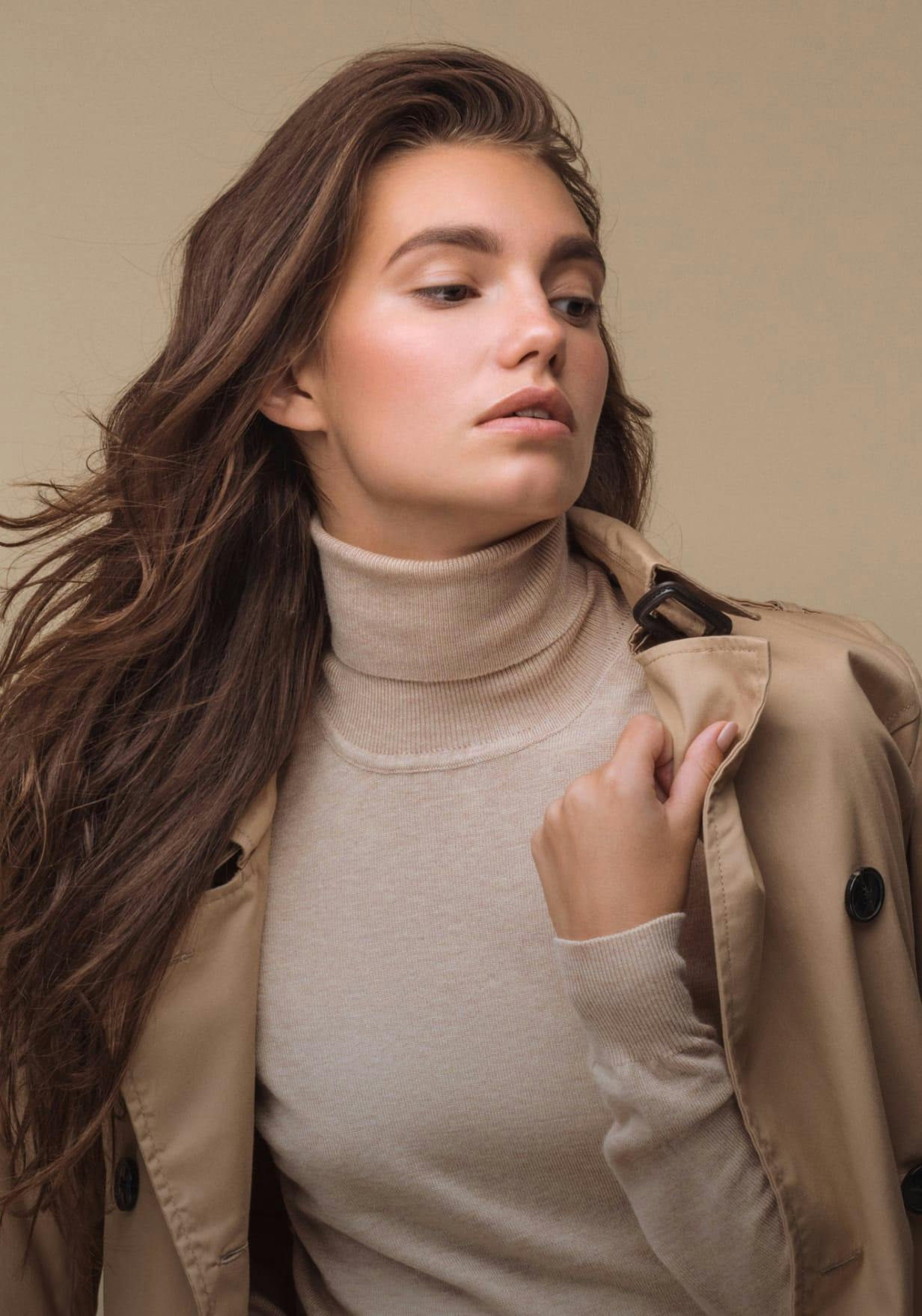 Glamourous woman with long brown hair wearing a beige top and coat