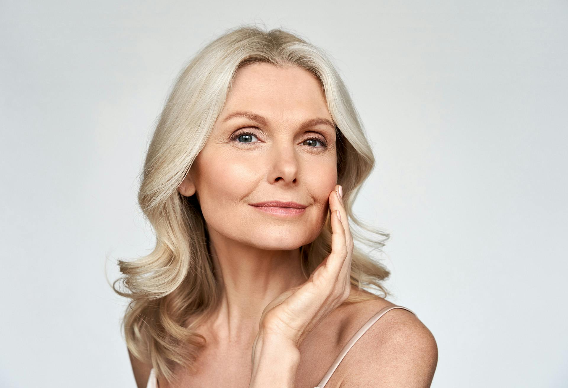 Beautiful older woman with curly blonde/grey hair touching her face