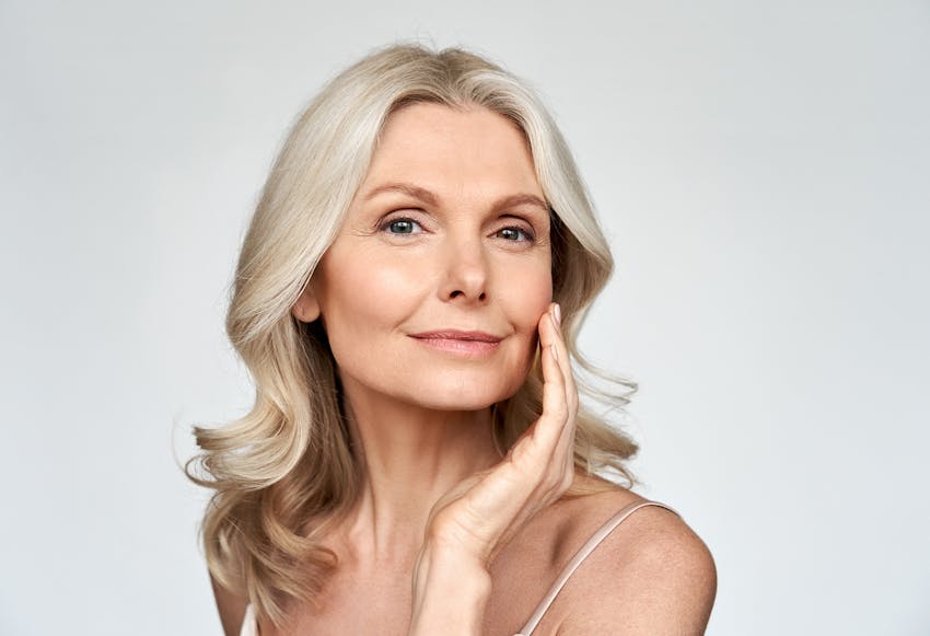 Beautiful older woman with curly blonde/grey hair touching her face