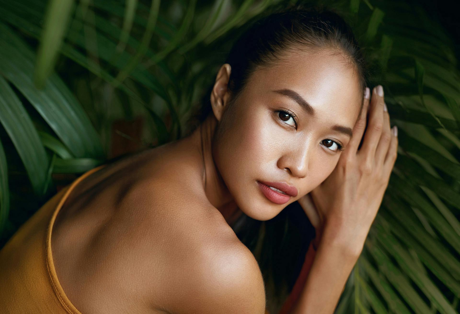 Woman in an orange top in front of a green plant