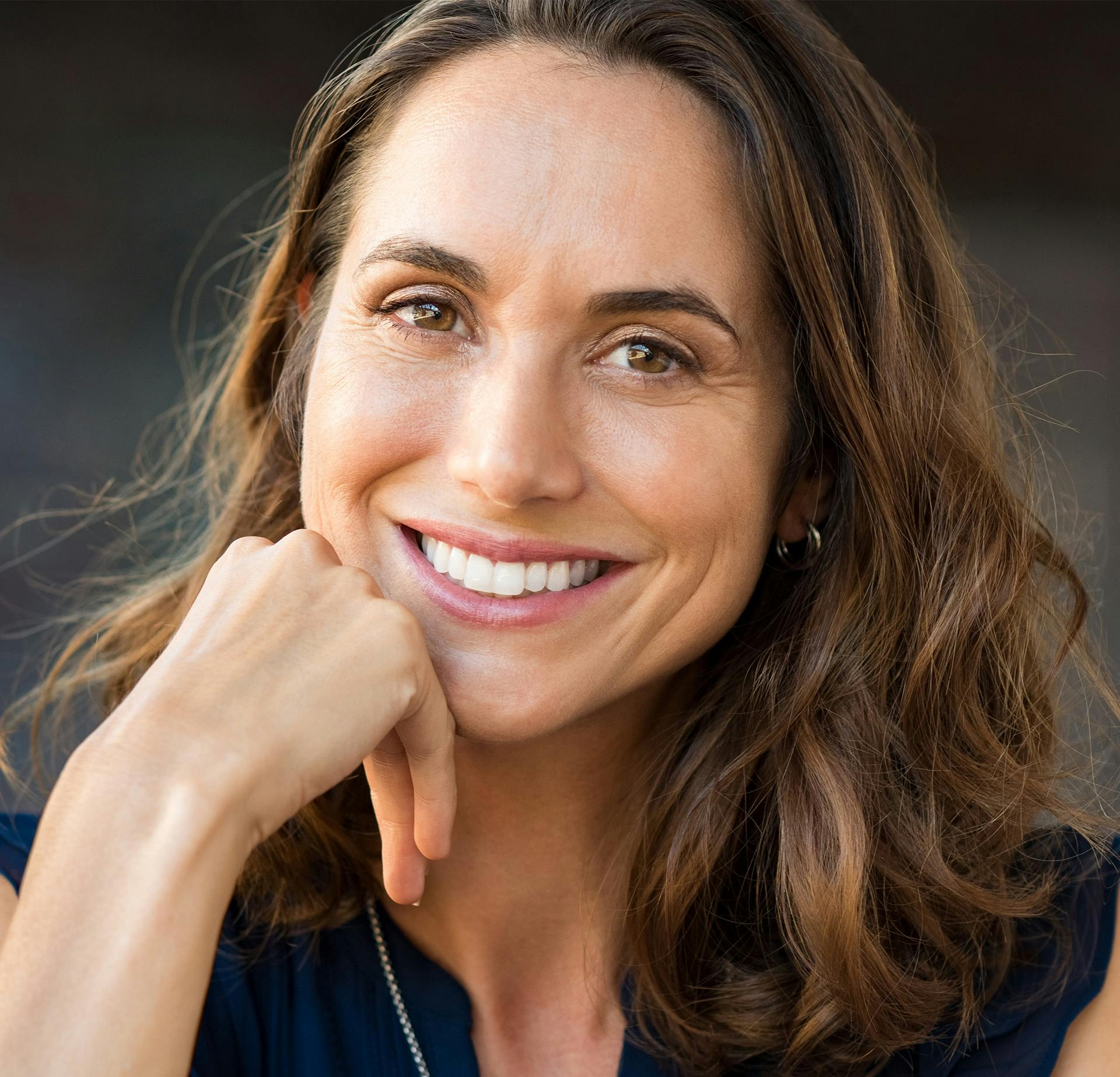 Woman with medium brown wavy hair smiling while resting her hand on her chin