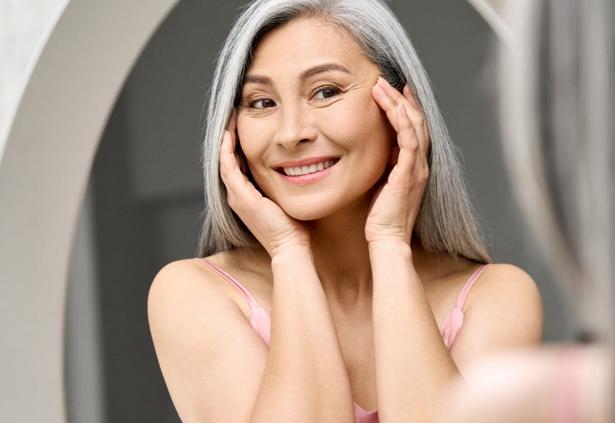 Woman with long gray hair smiling looking in the mirror