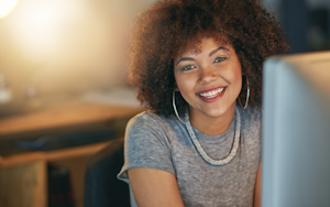 A woman smiles at the camera from behind a computer screen 