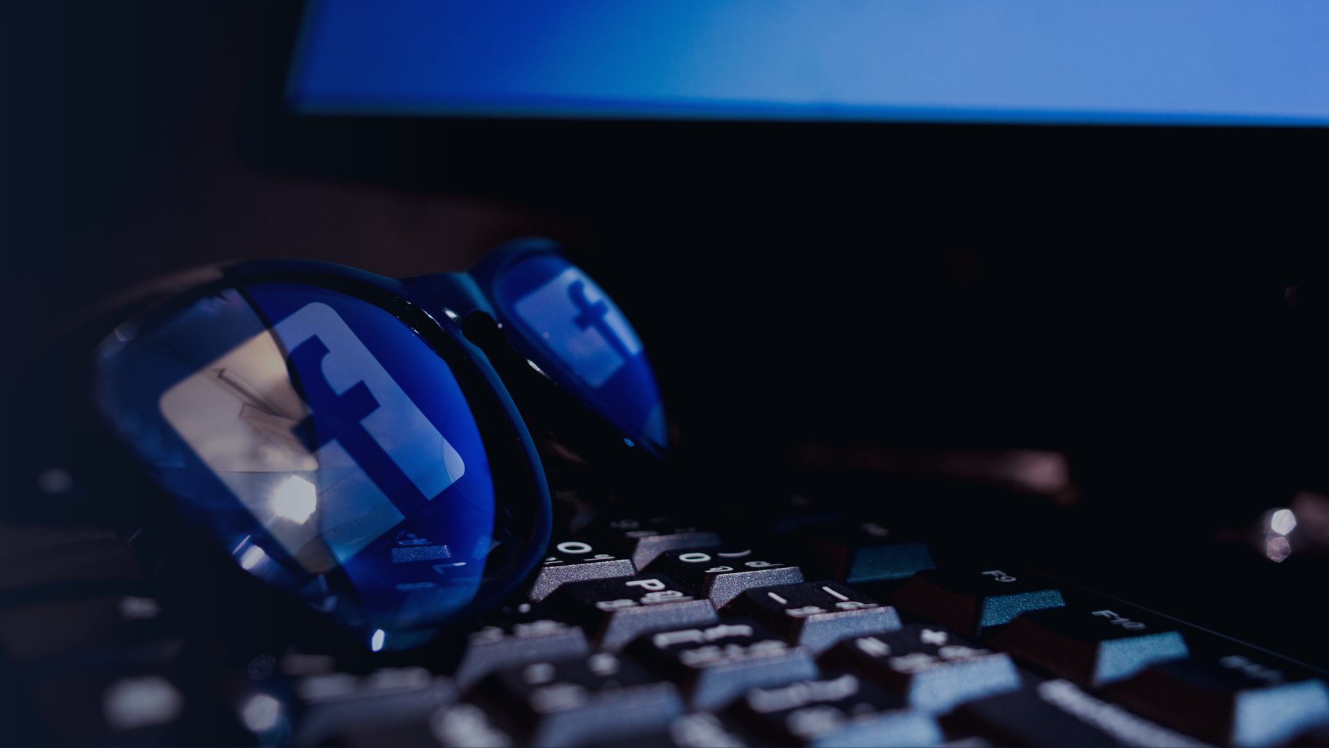 Glasses lying on a computer keyboard, reflecting the Facebook logo.