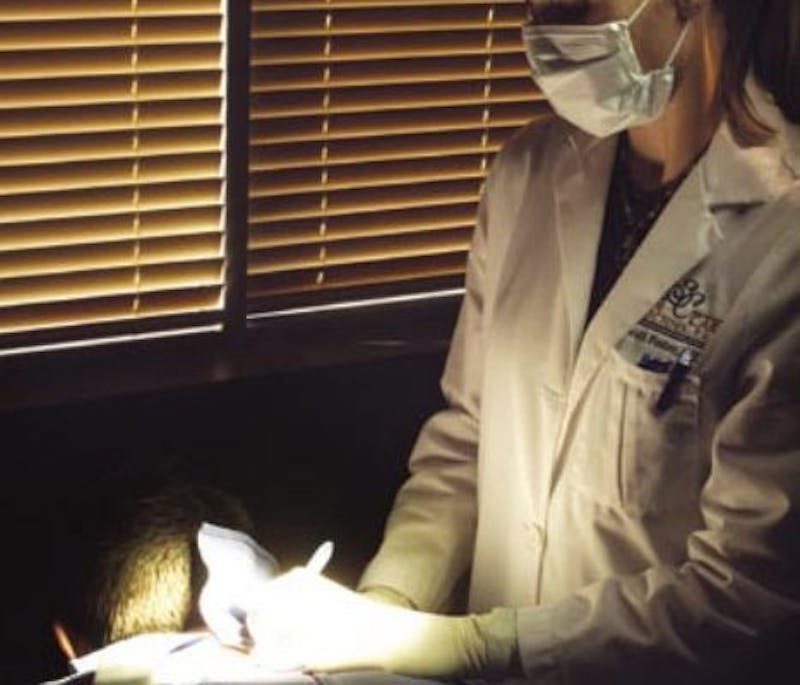 Dr. Heidi Foster in a white lab coat and mask sitting in a chair
