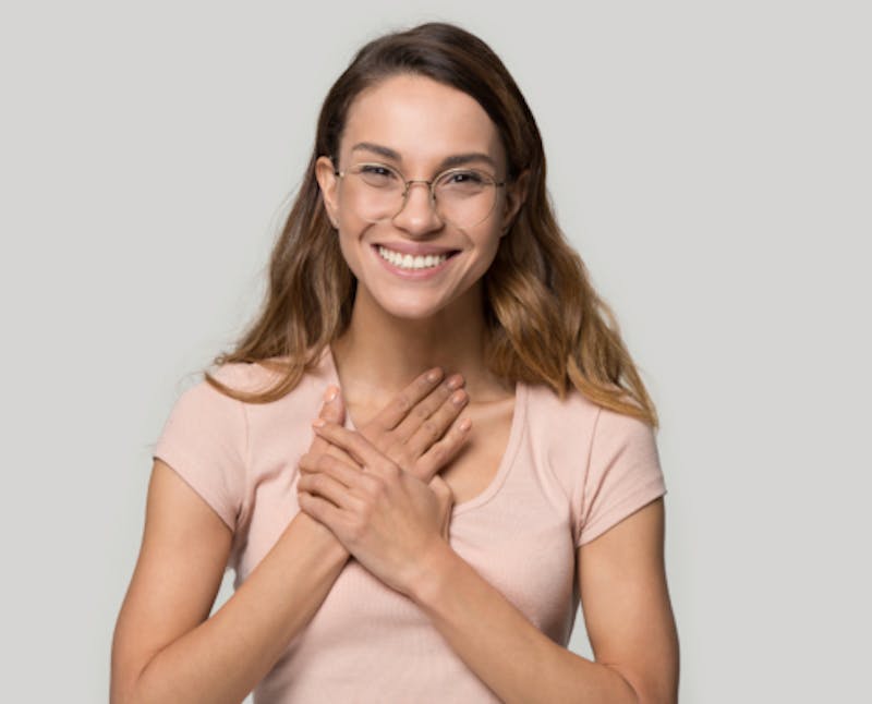 smiling woman with glasses and pink shirt holding her hands together