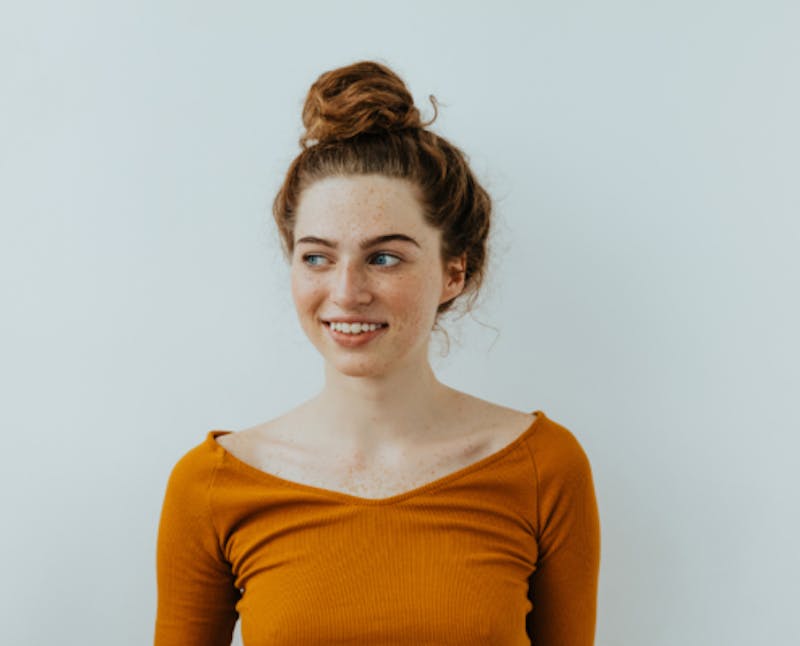 woman with a bun in her hair smiling and reddish brown top