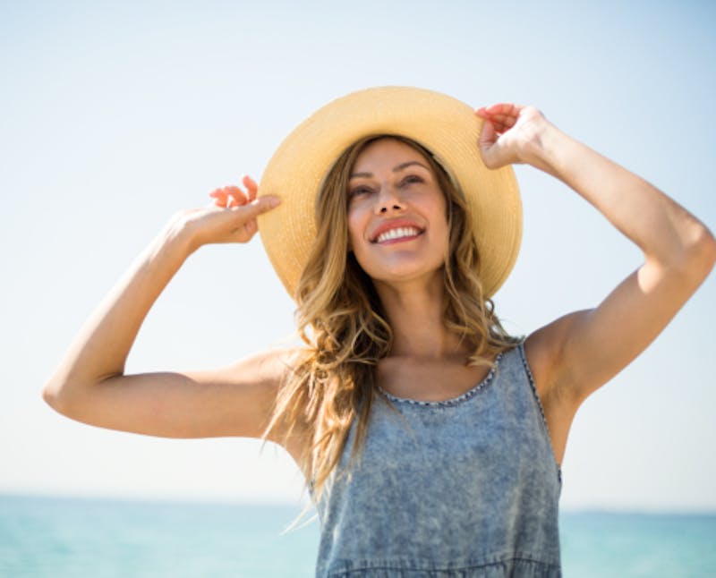 woman in a hat standing on the beach with her hands on her hat