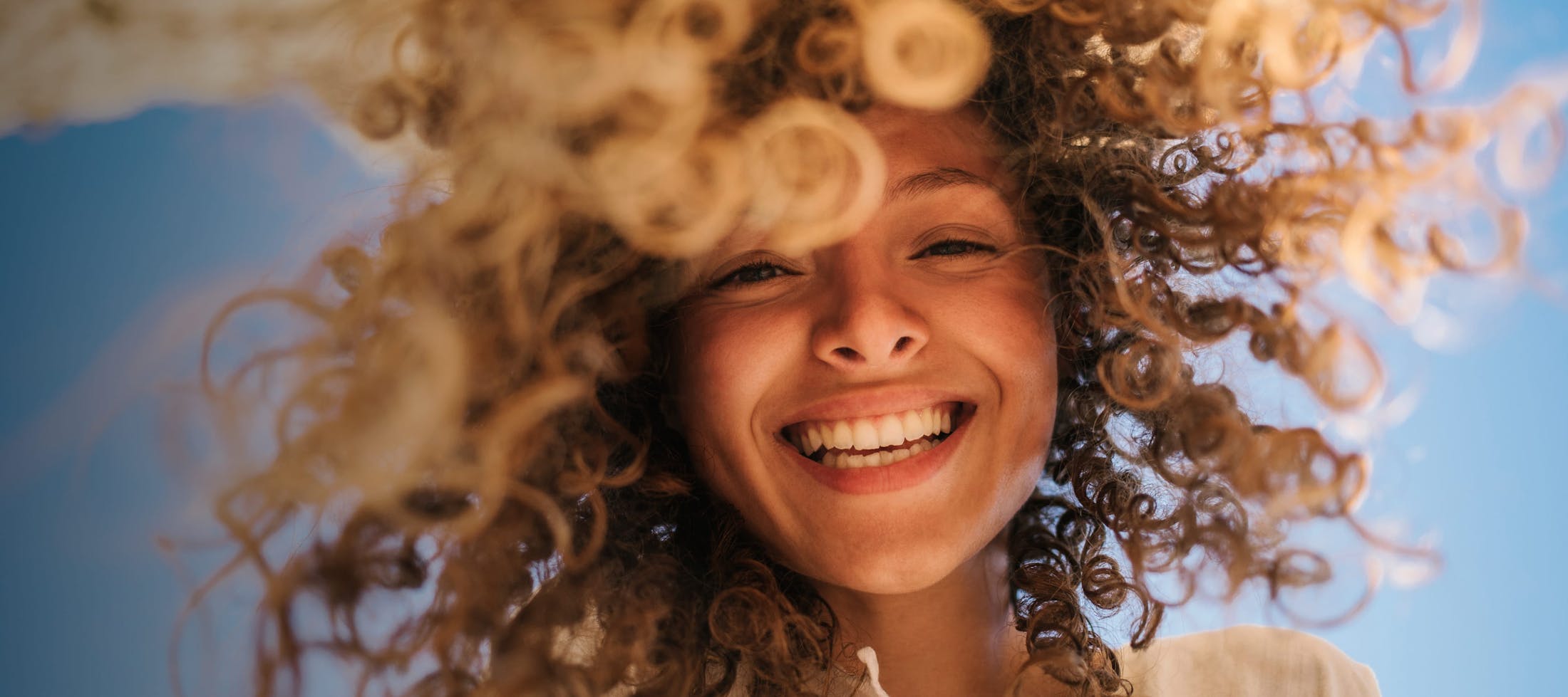 Pretty girl with very curly hair looking down smiling big