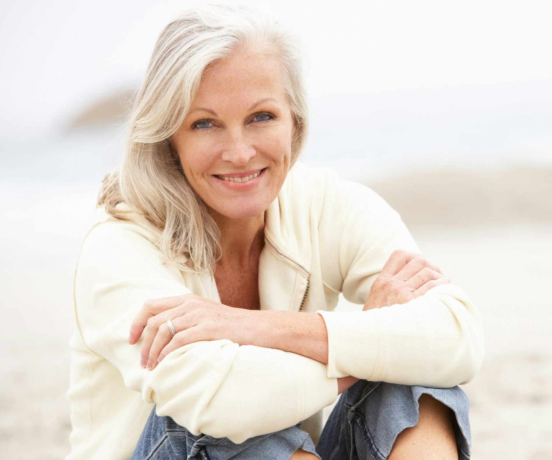 Older woman sitting on the beach in a cream colored sweater