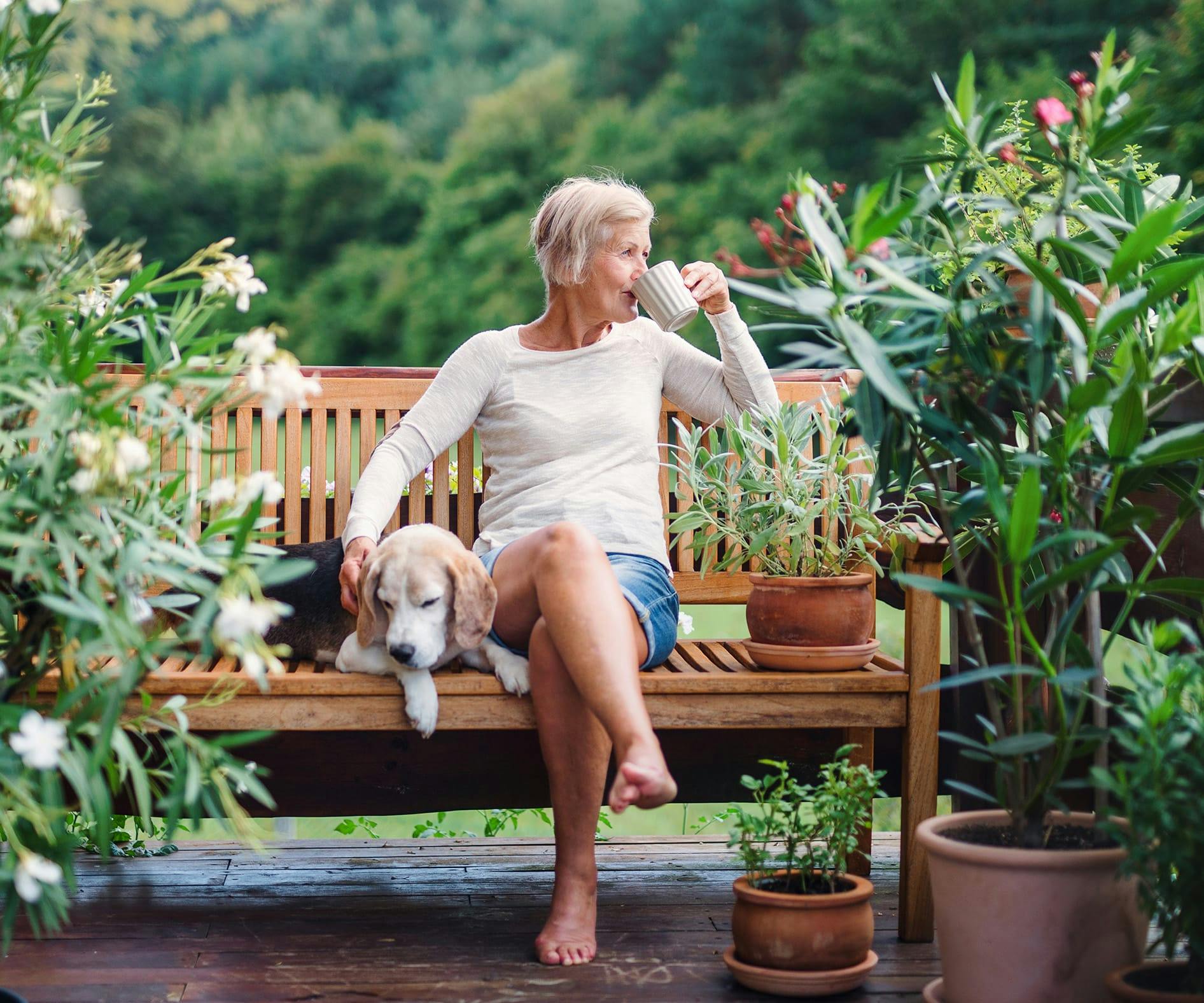 Woman sitting on a bench drinking coffee with a dog next to her