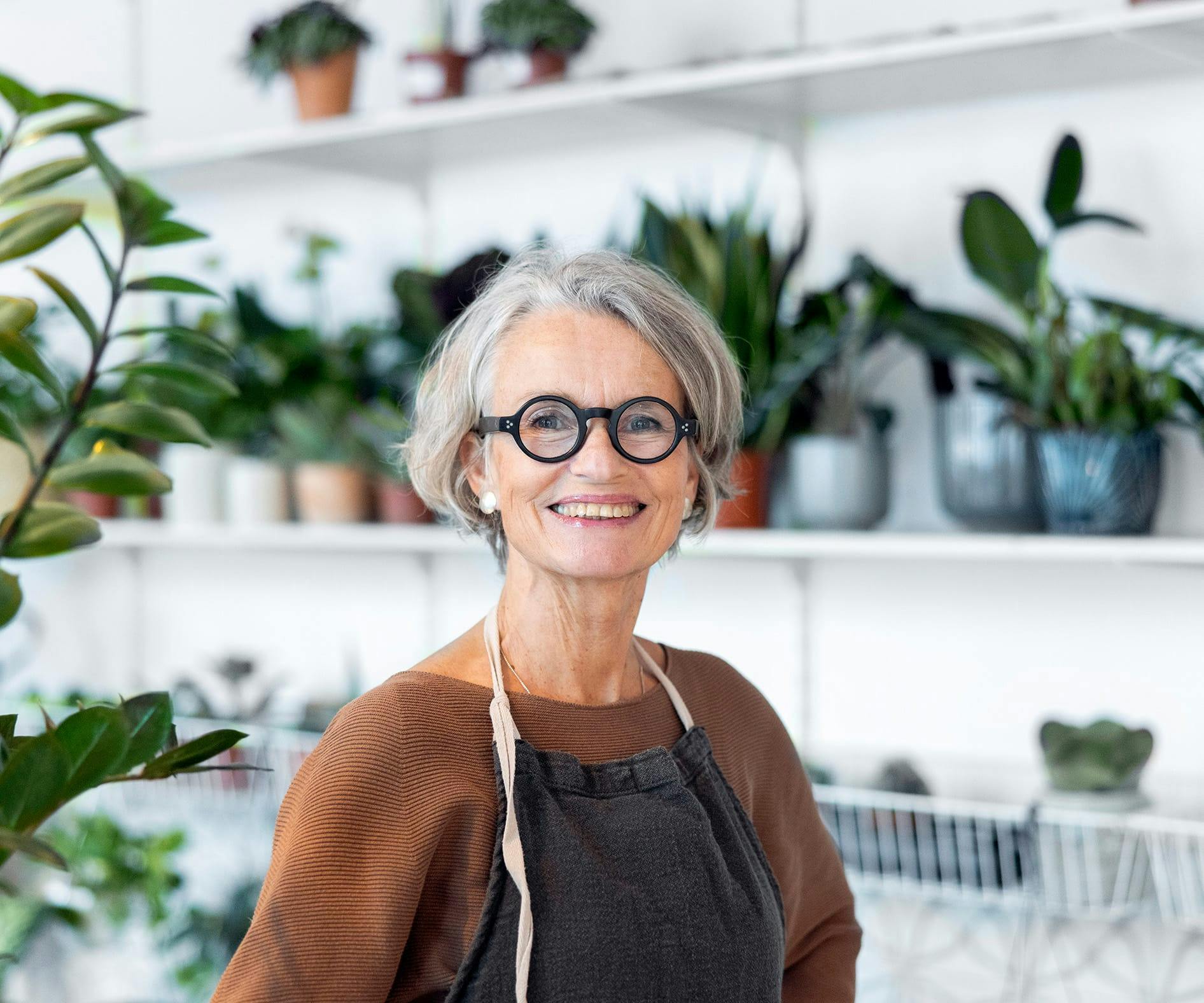smiling woman in glasses standing in front of a shelf of plants