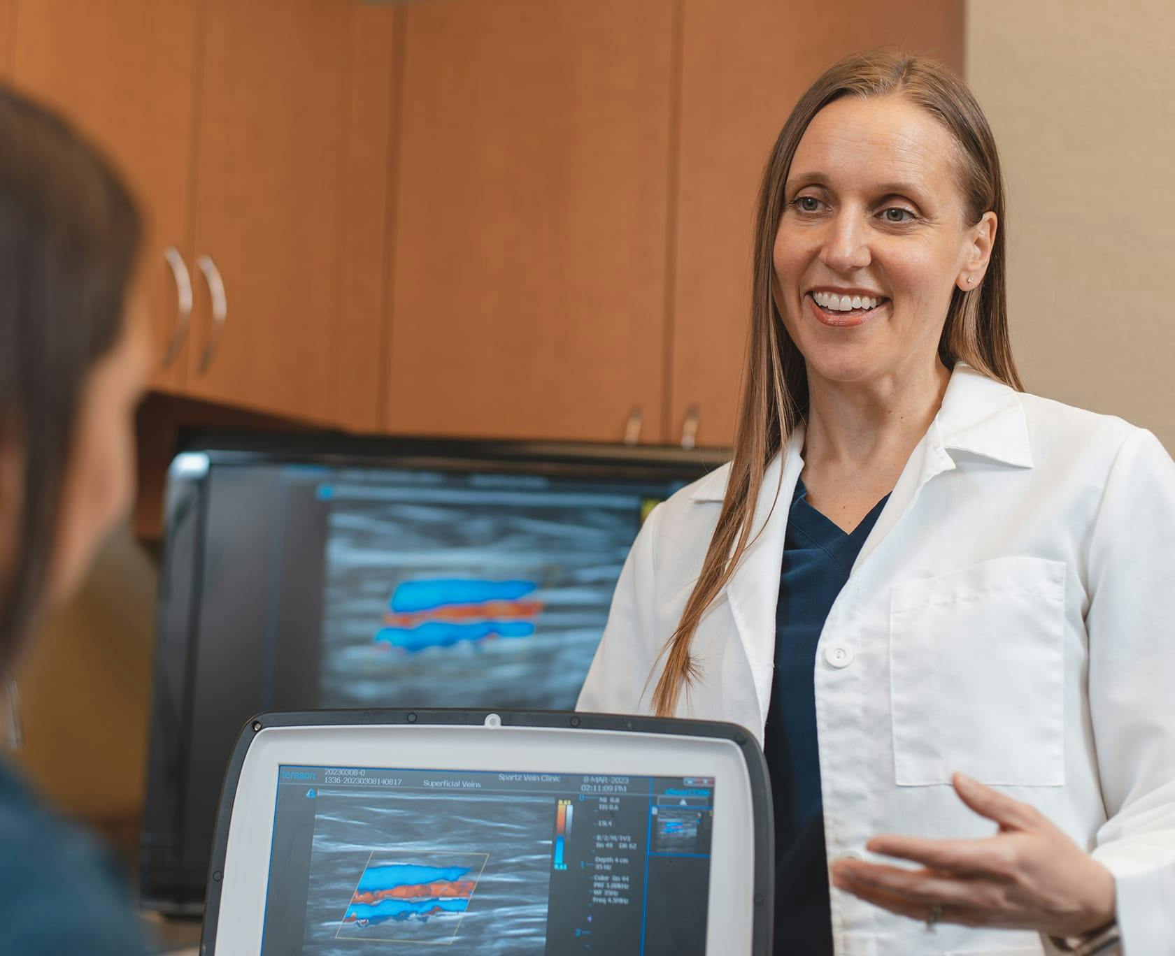 woman in white lab coat talking to a woman in front of a computer