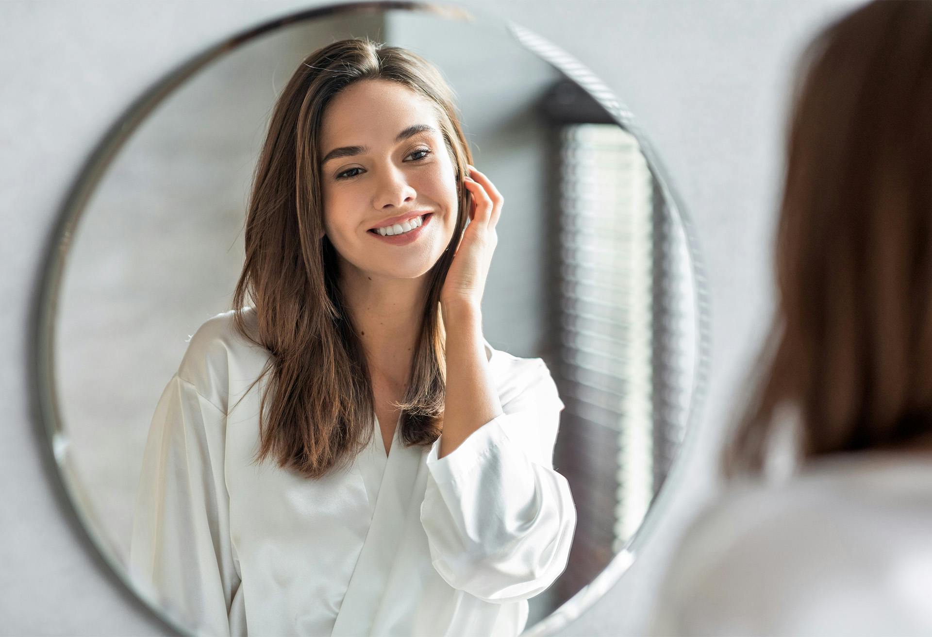 woman in white shirt looking at herself in mirror
