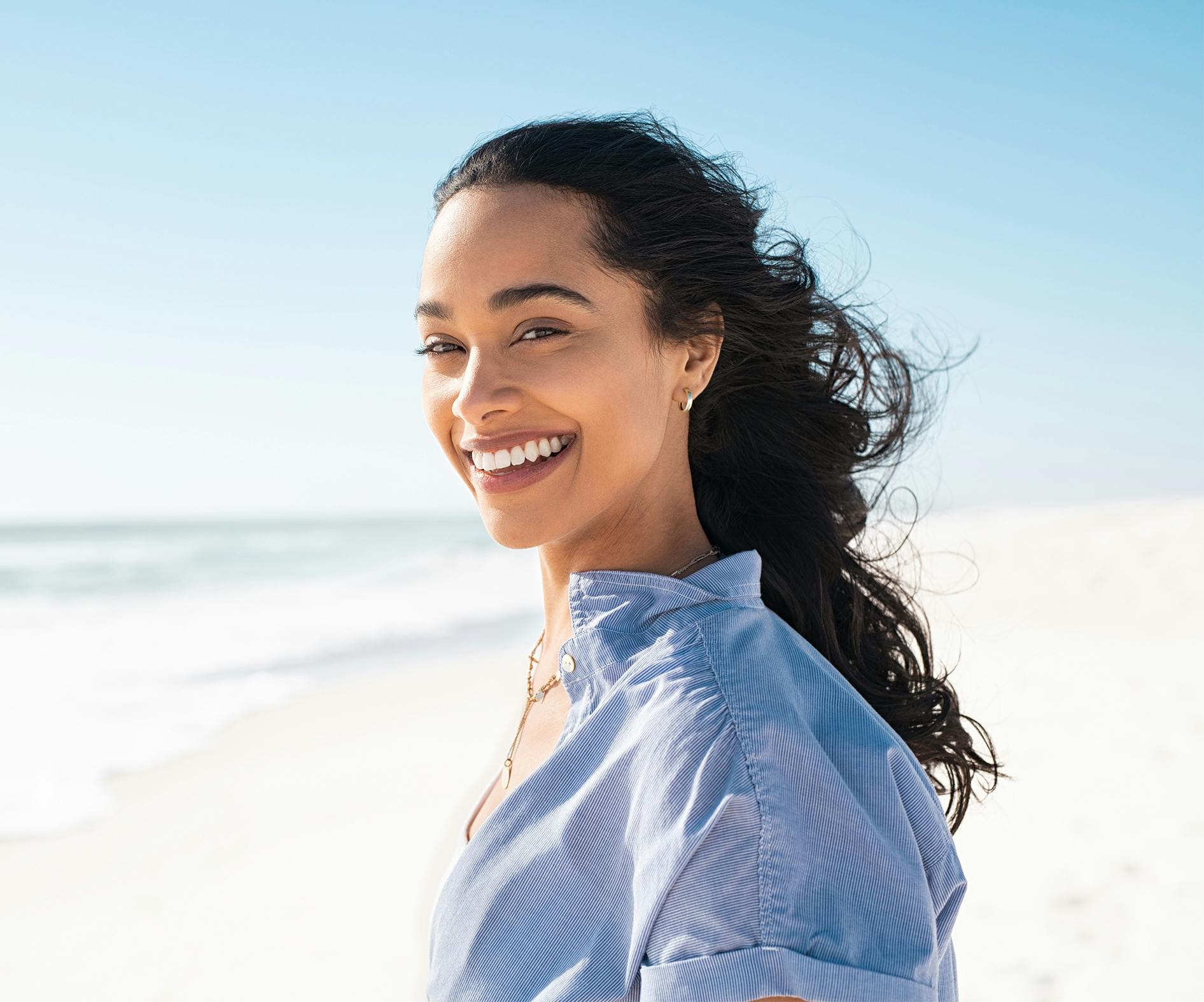 smiling woman on the beach with a blue shirt and white sand