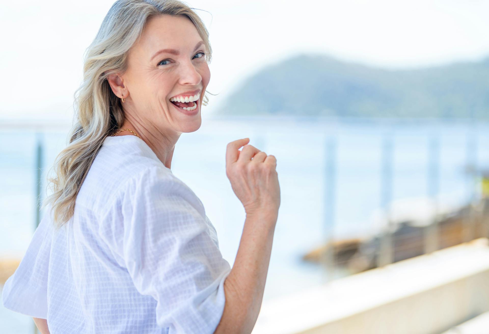 smiling woman in white shirt standing on a balcony near the water