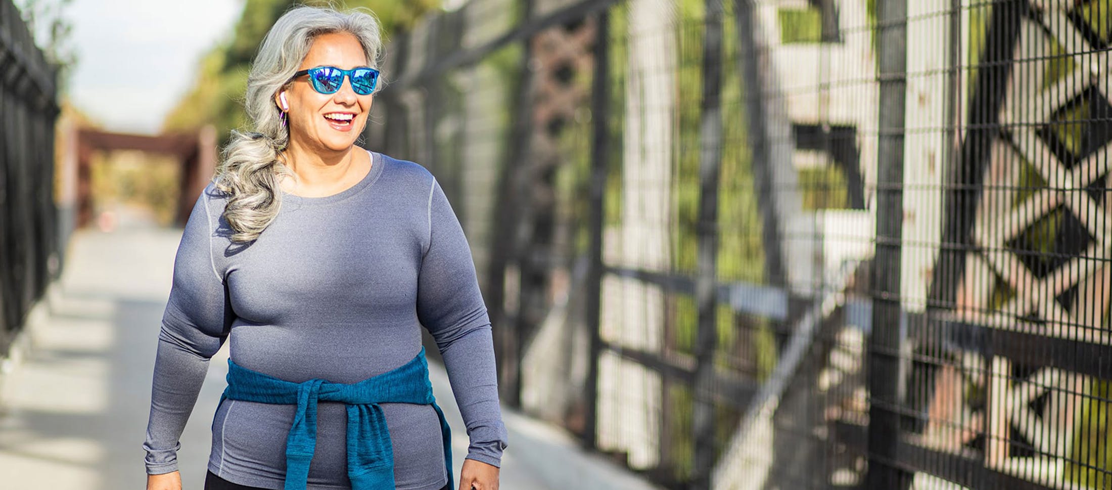 smiling woman in sunglasses walking down a sidewalk