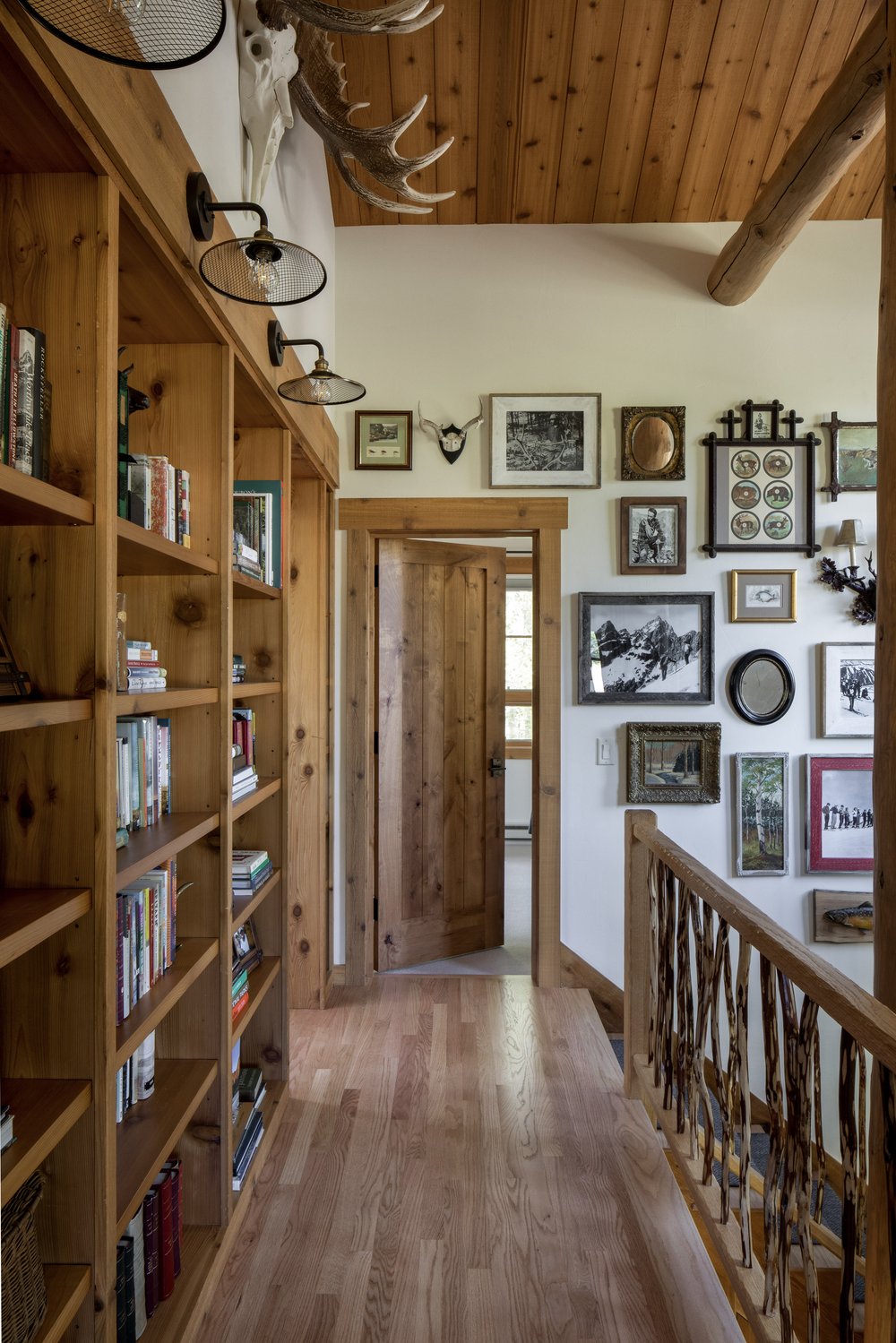 Wood built in bookshelf in a hallway with a picture wall showcasing western cabin like decor