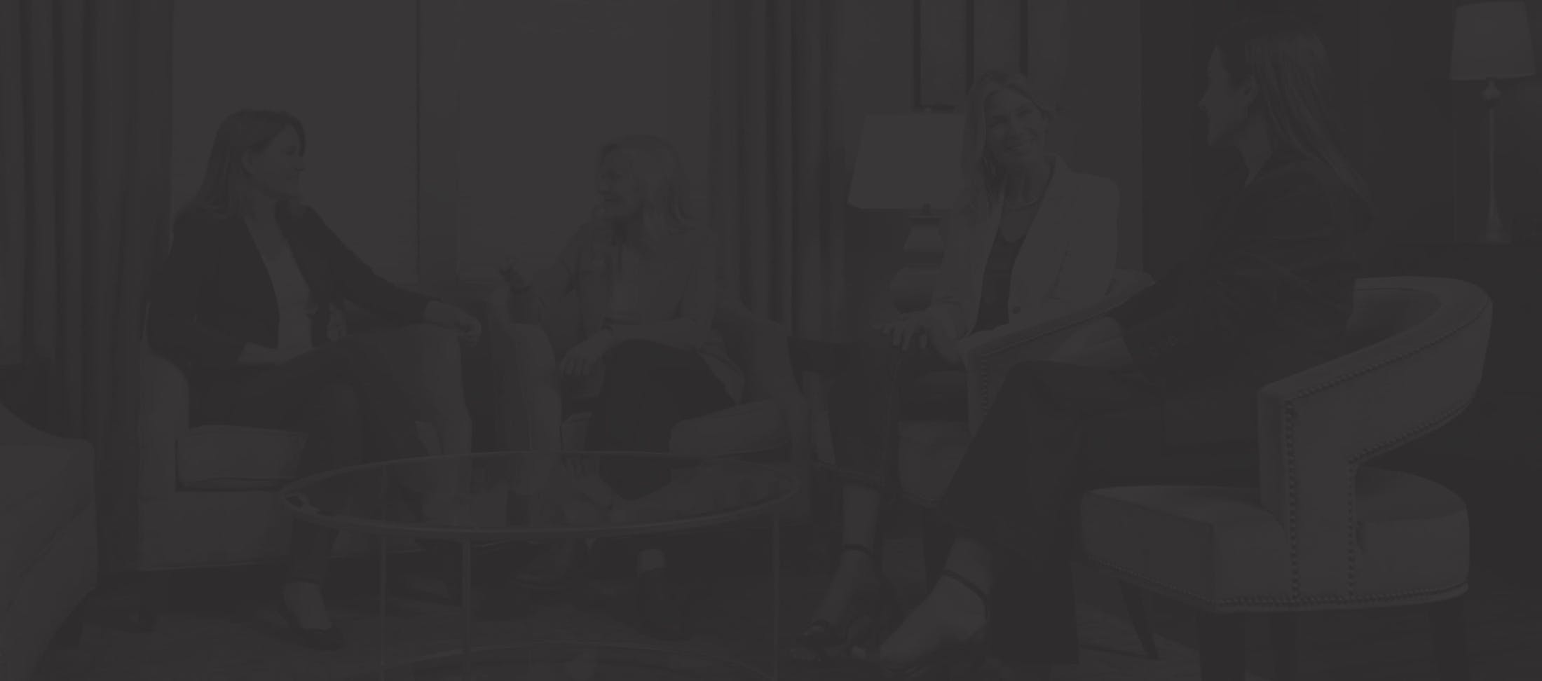 A very faded image of four women talking while sitting on chairs