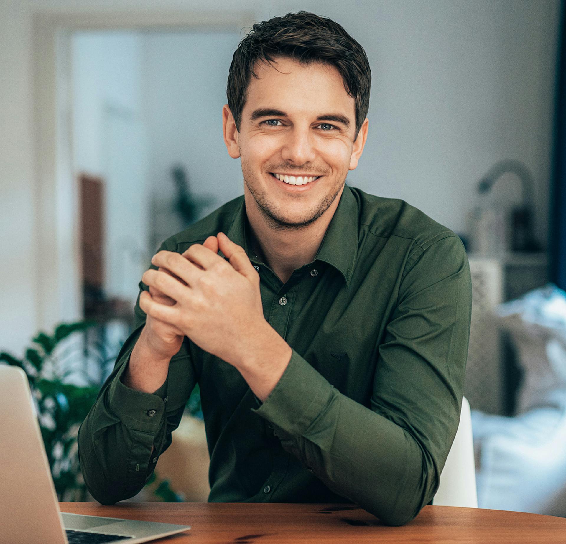 Man in a green shirt smiling while sitting in front of a laptop