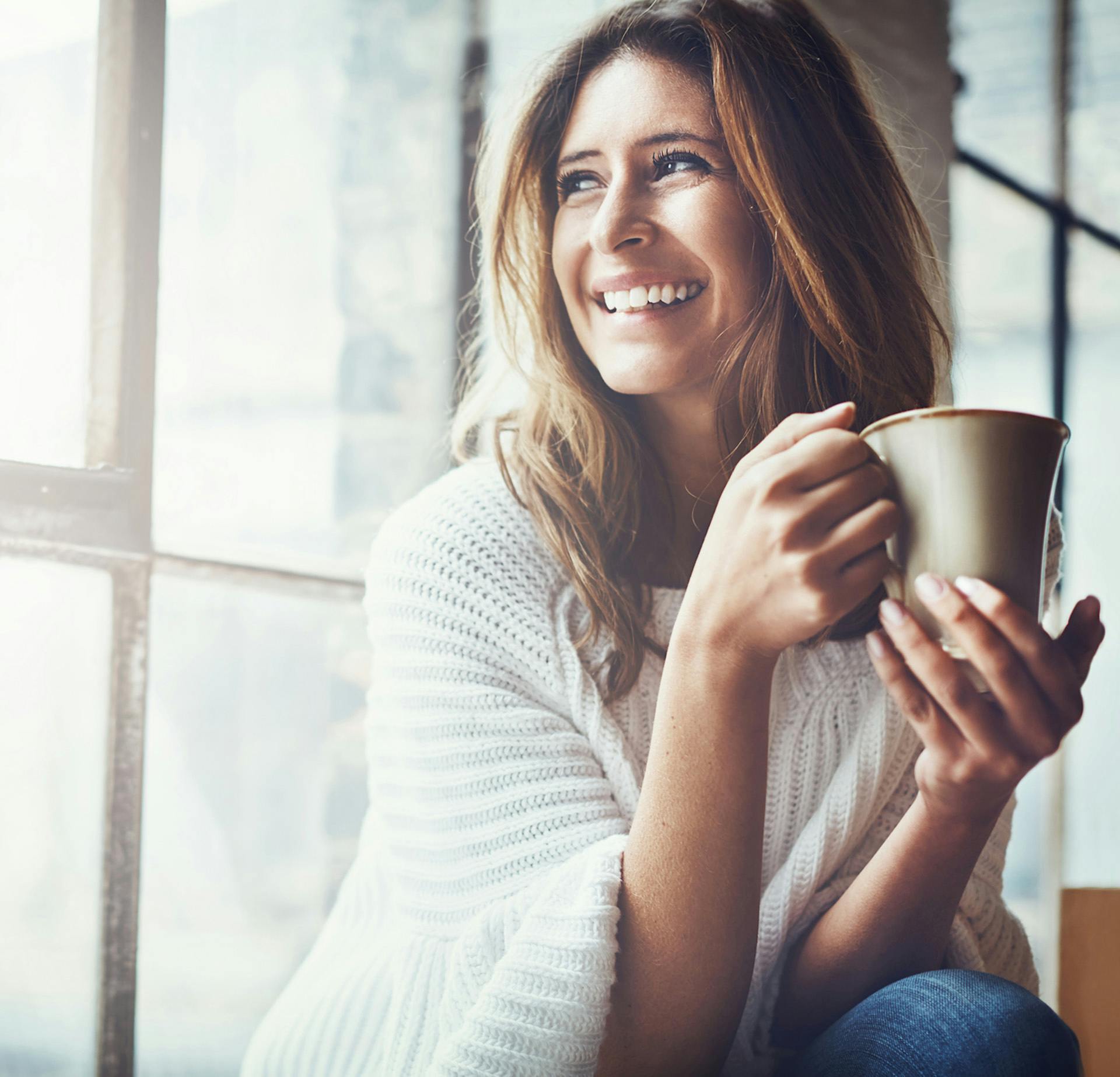 Woman with a coffee in her hand sitting in front of a window