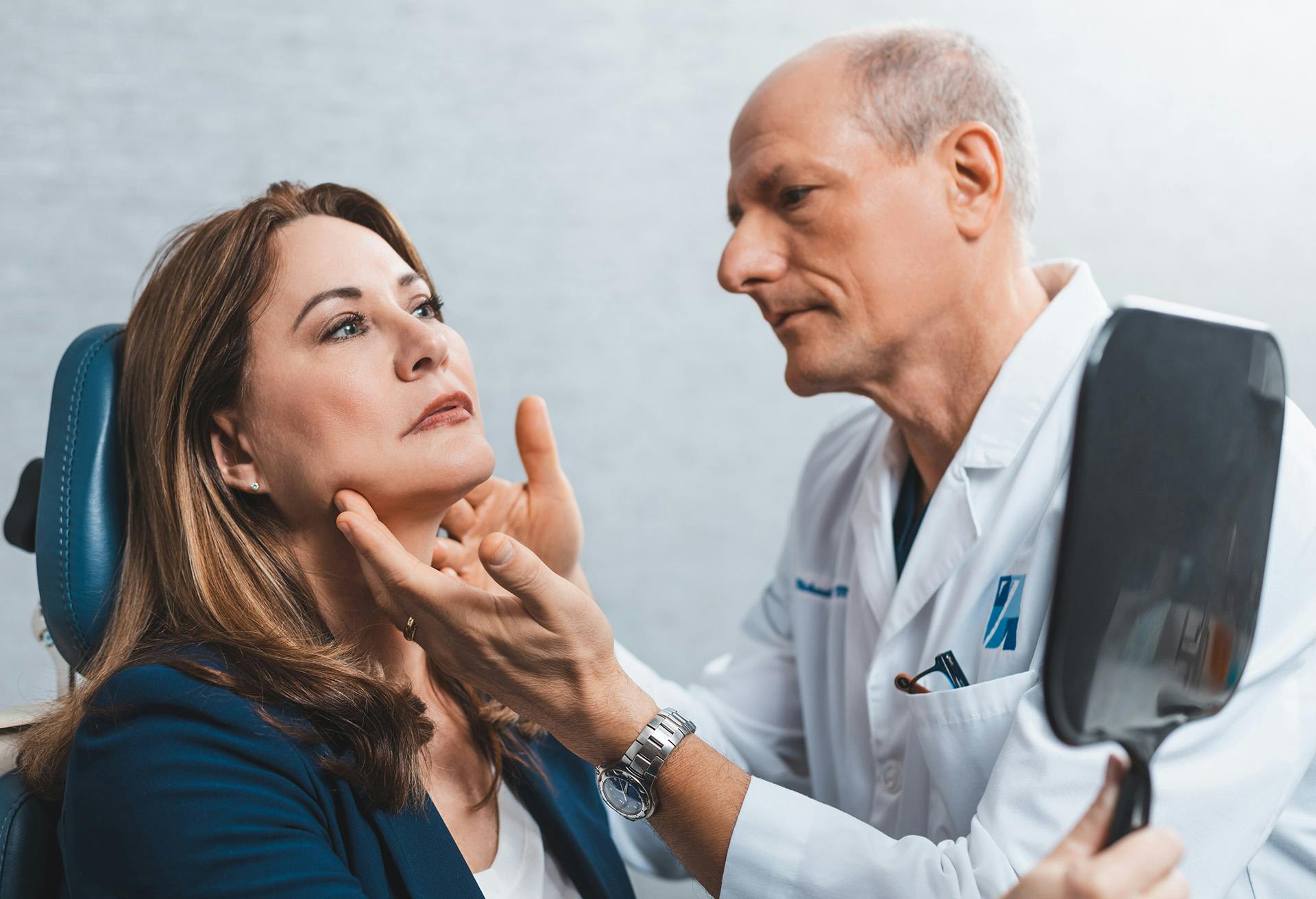 Dr. Zenn looking at a womans neck and chin as she looks into a mirror