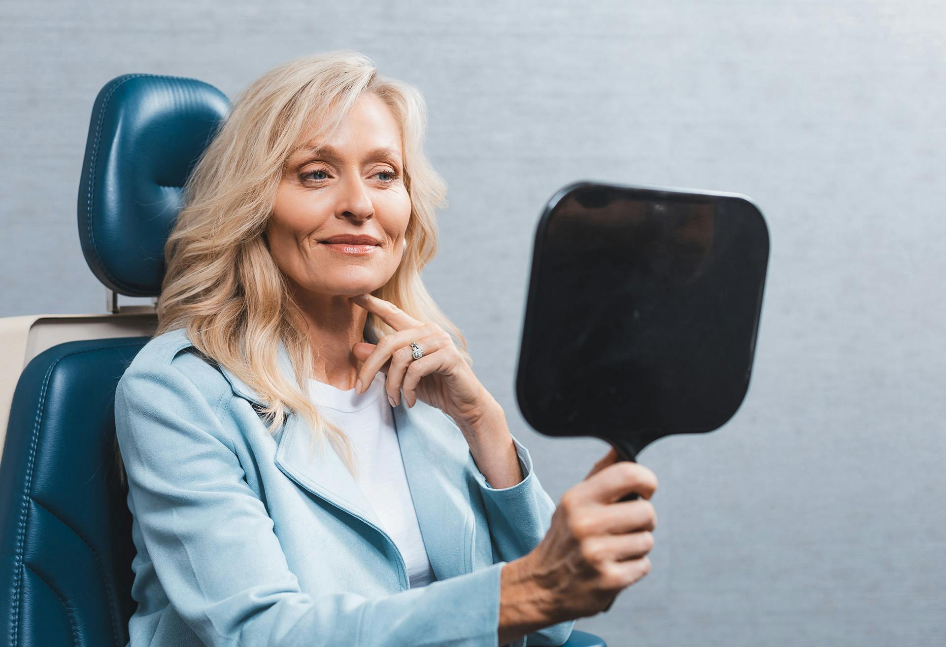 Woman sitting in a chair with a mirror in her hand looking into it