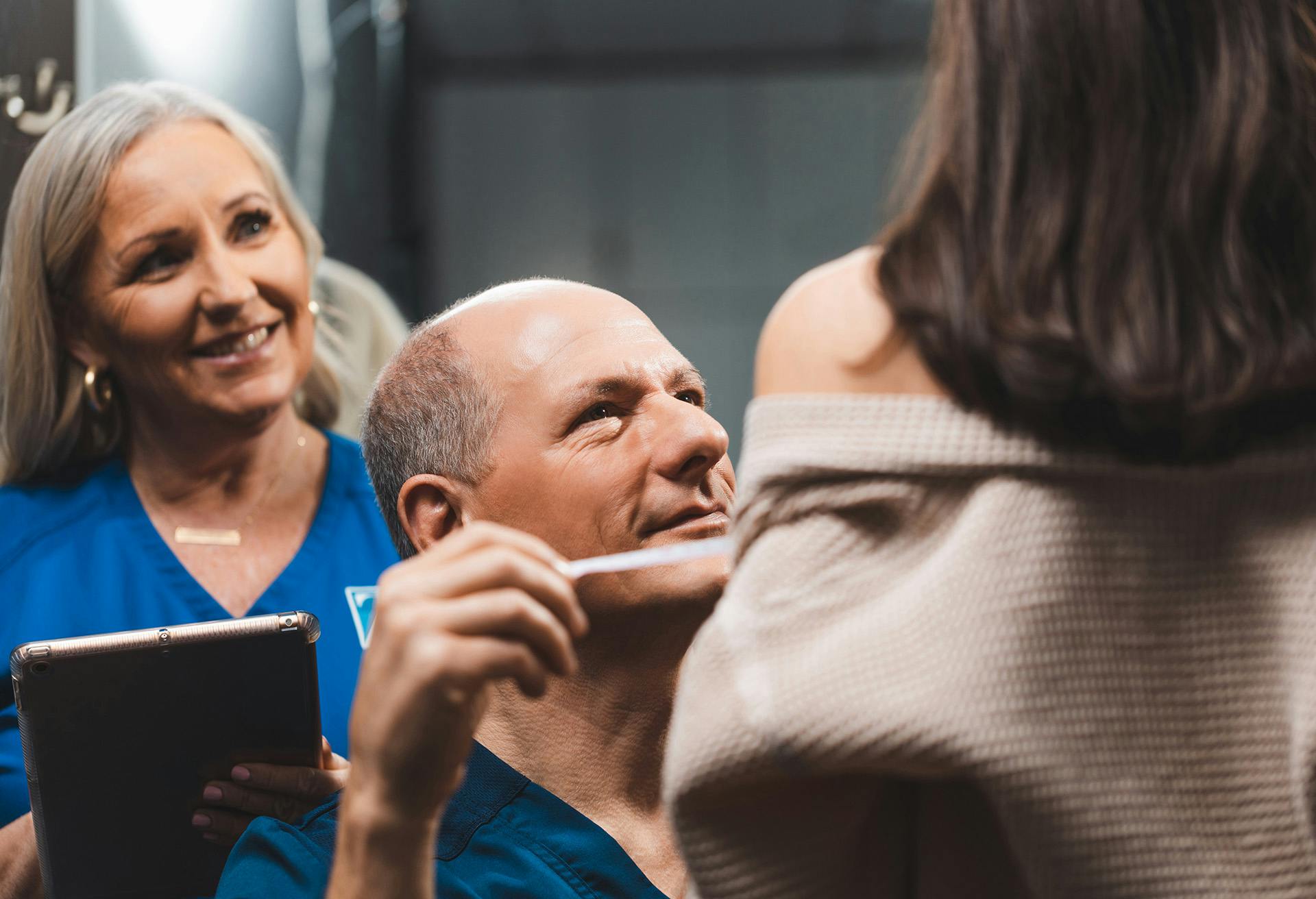 Dr. Zenn examining a patient with a nurse behind him on an ipad