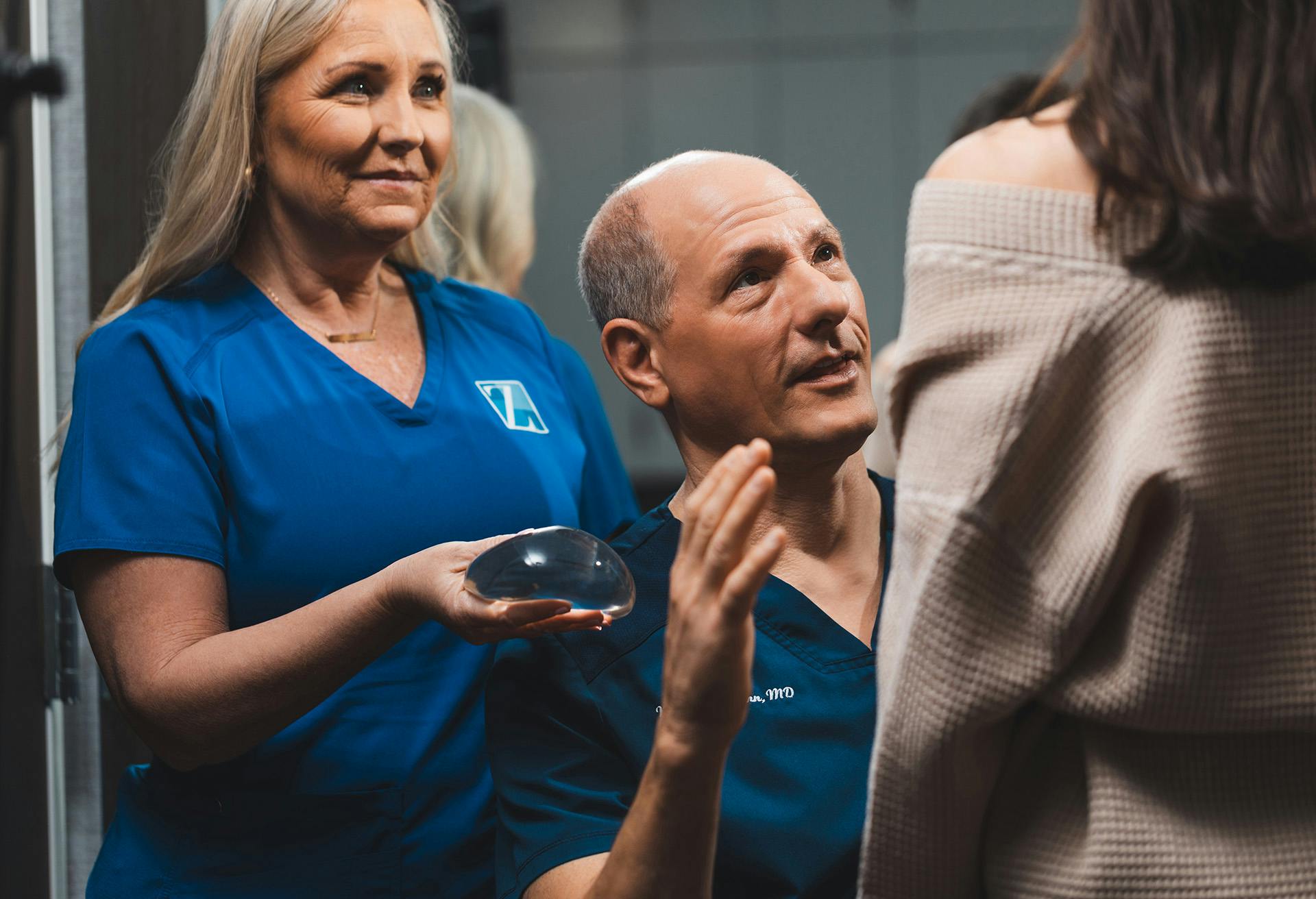 Dr. Zenn looking at a patient with a nurse behind him holding a breast implant
