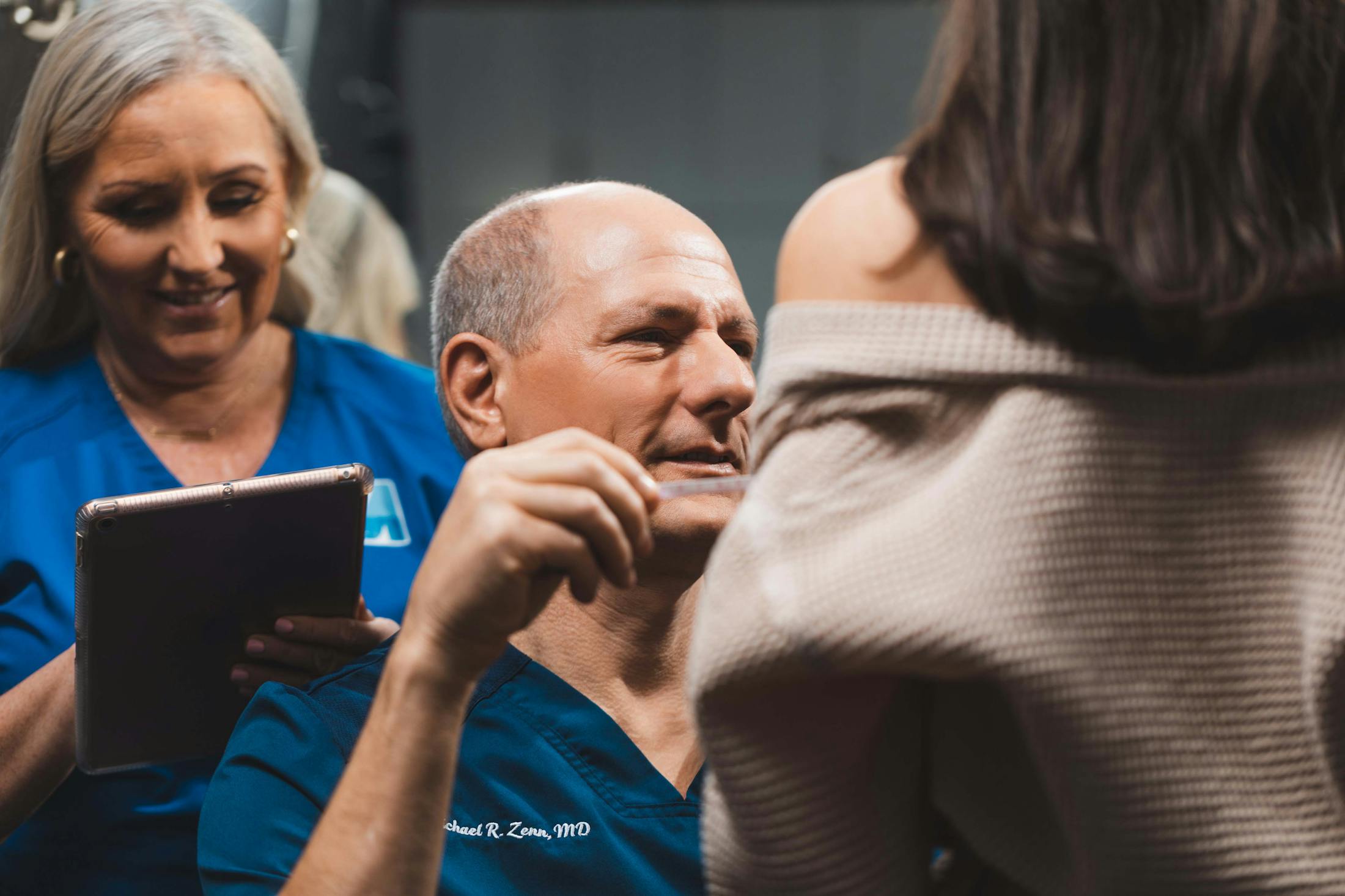 Dr. Zenn examining a patient with a nurse behind him on an ipad